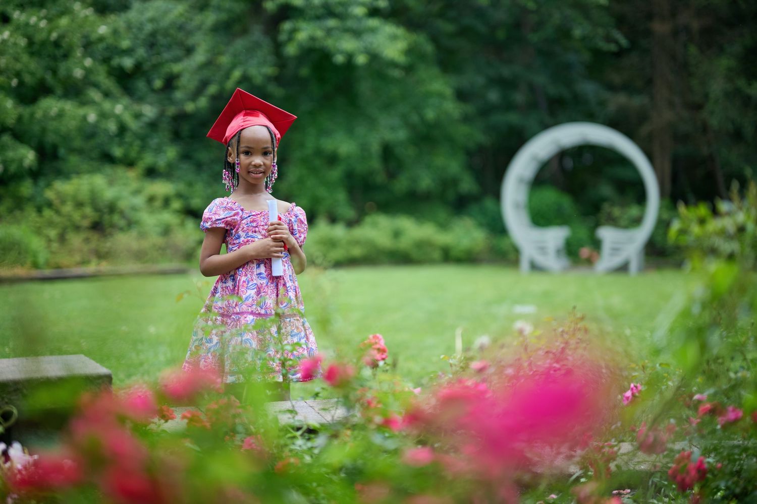 Graduation photo session in lush garden with pink flowers in foreground.