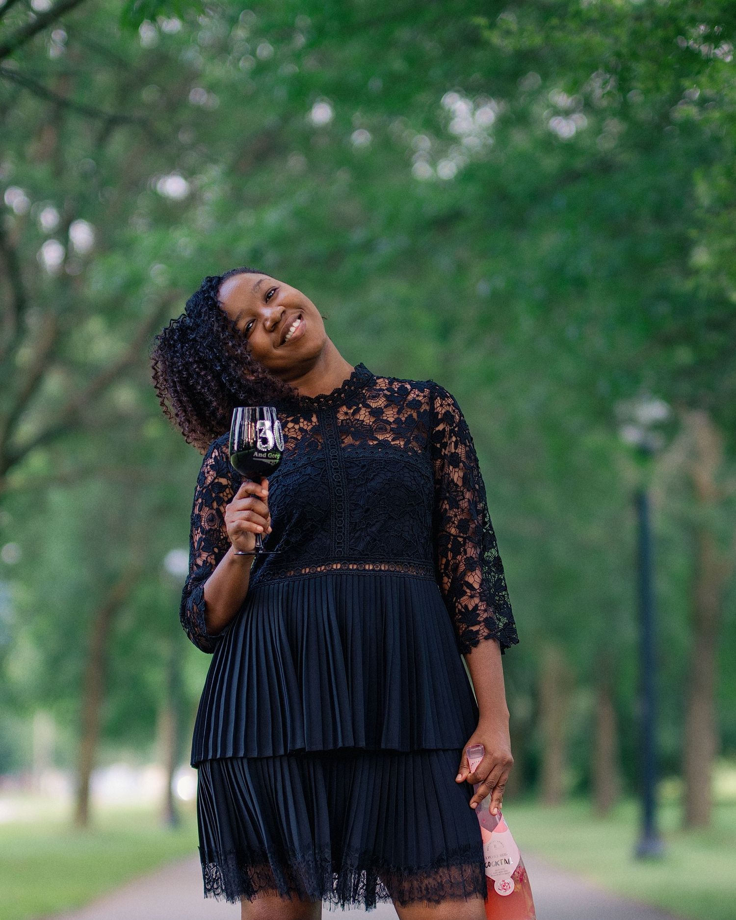 Person in a black lace dress twirls playfully in a green park setting.