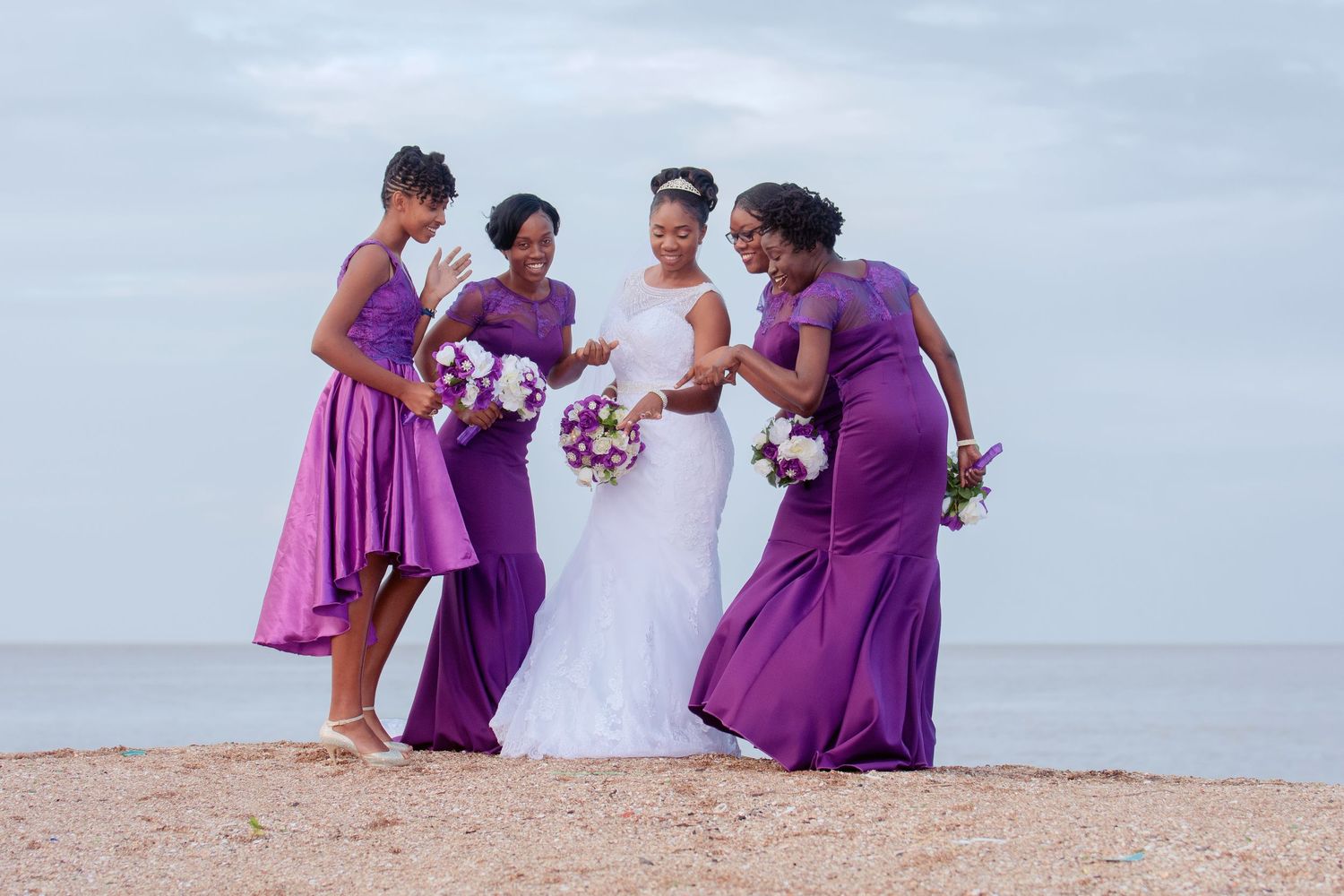 Wedding party in purple dresses laughing together on a beach.