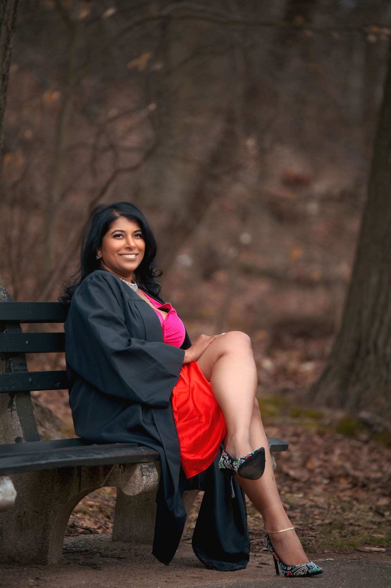 Graduation portrait session on wooden bench surrounded by autumn foliage.