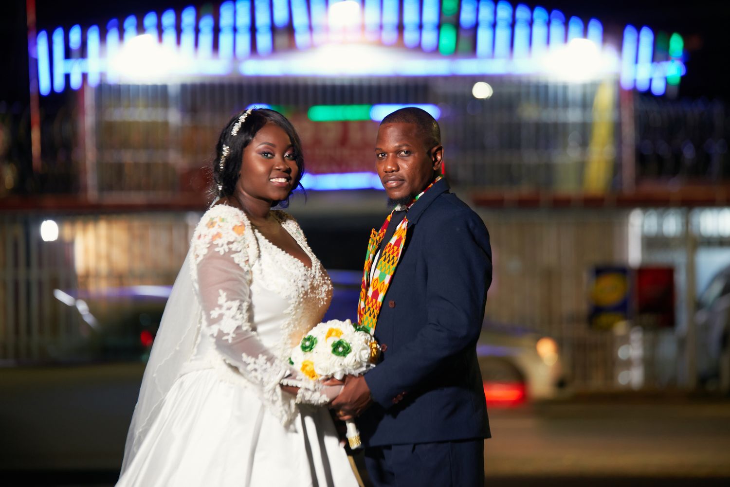 Couple dancing together at an evening wedding reception with colorful lights in the background.