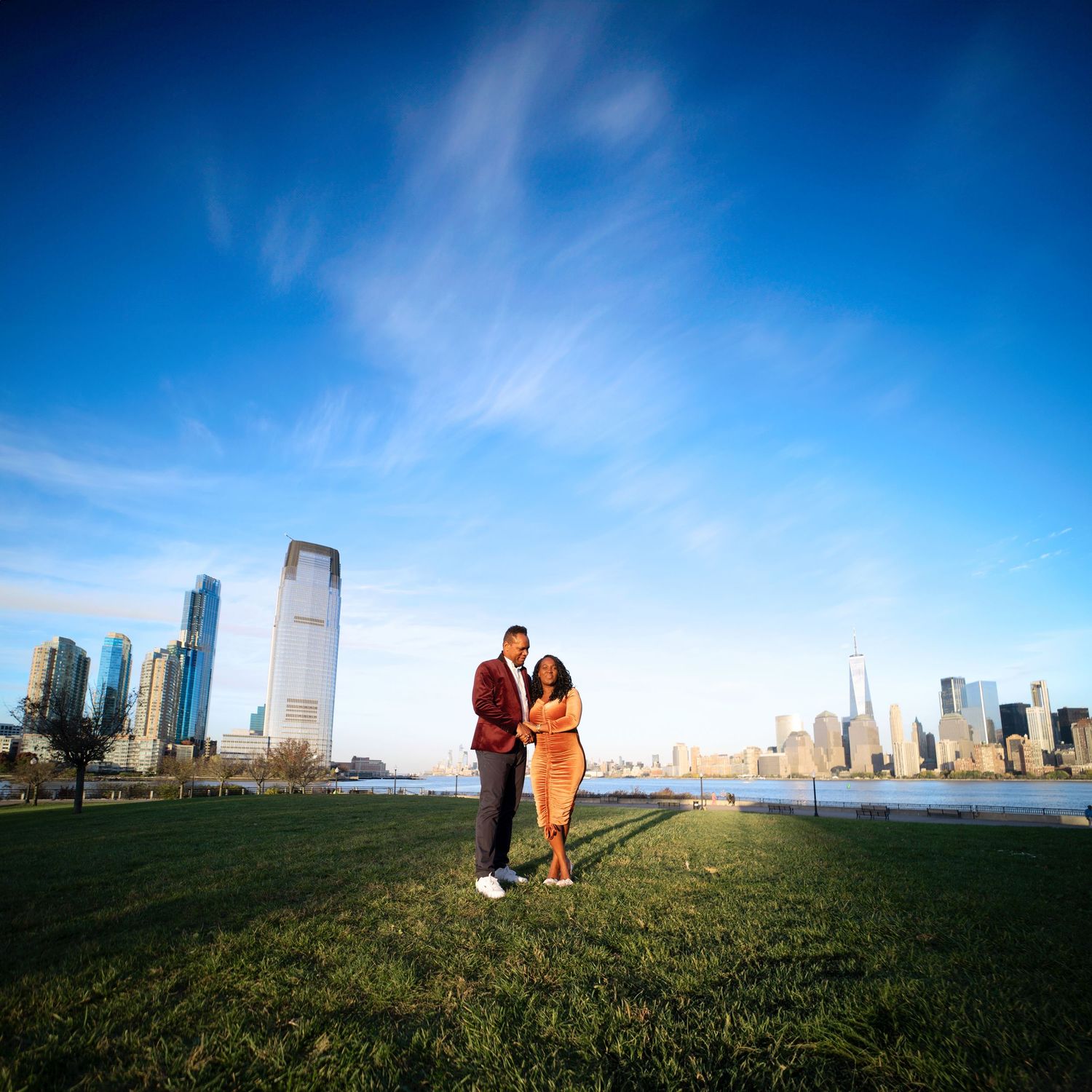 A couple poses against a dramatic wide-angle view of the New York City skyline.