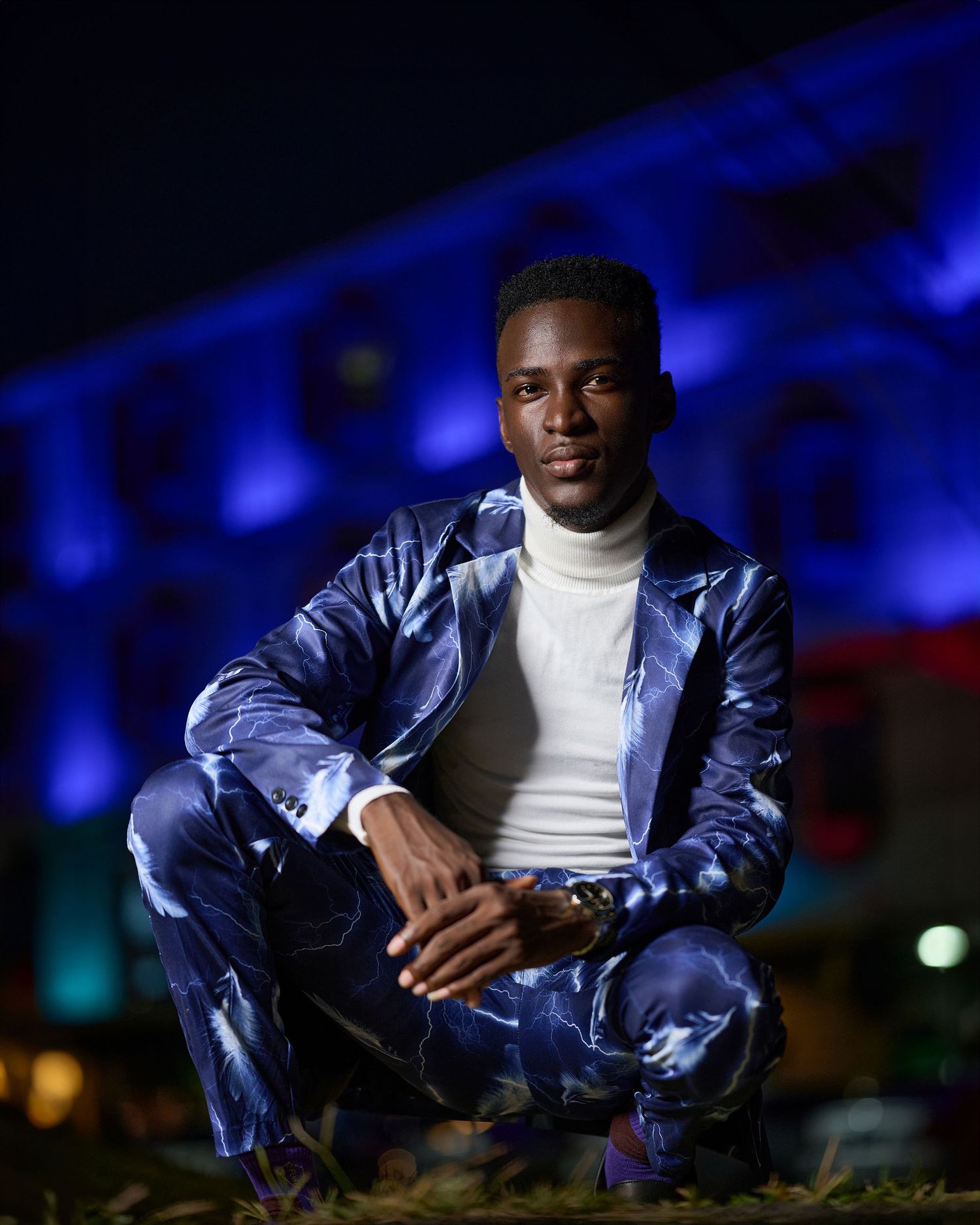 Dramatic nighttime portrait in white turtleneck and metallic blue jacket with dark lighting.