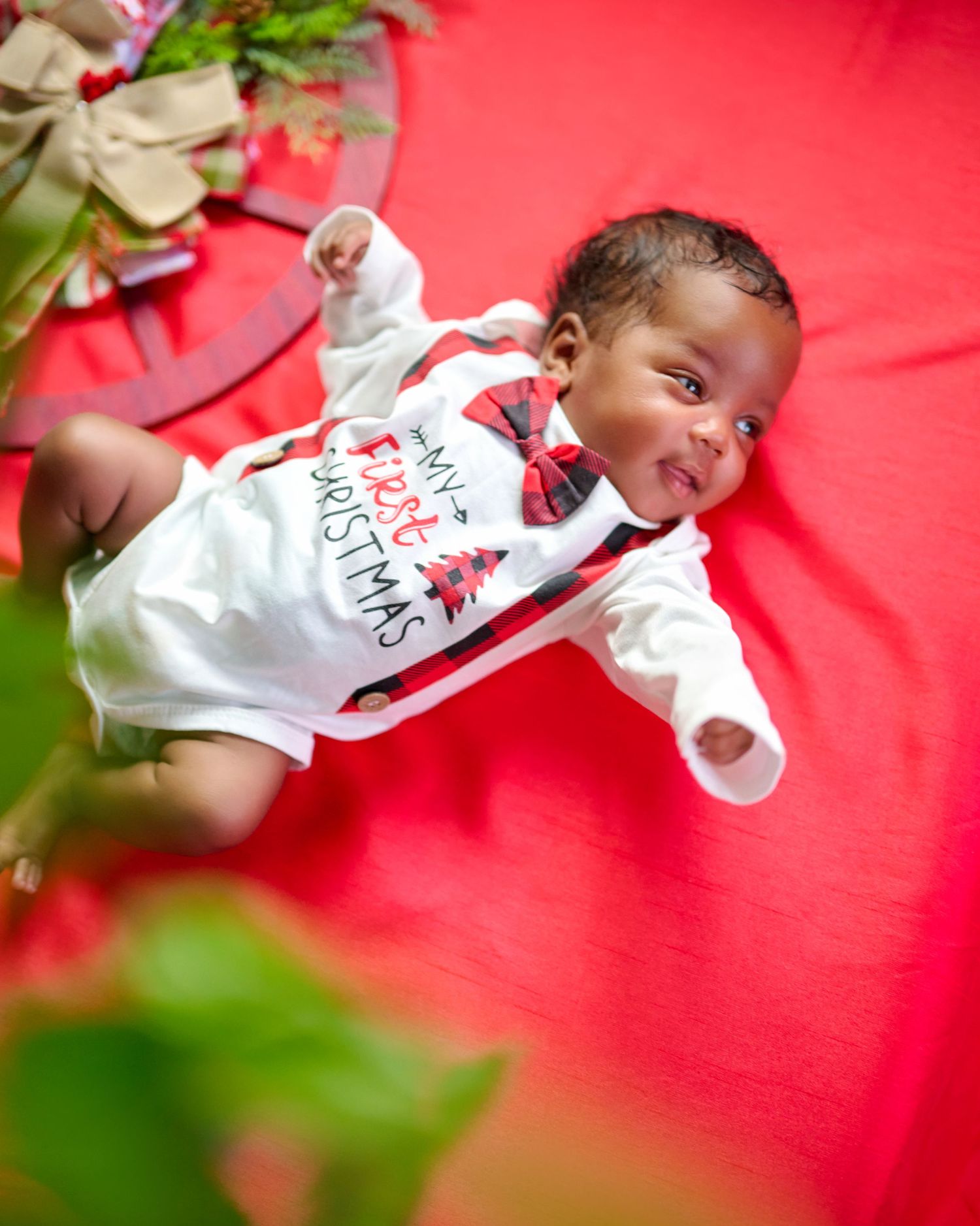 Festive baby portrait on bright red background with holiday greenery and decorations.