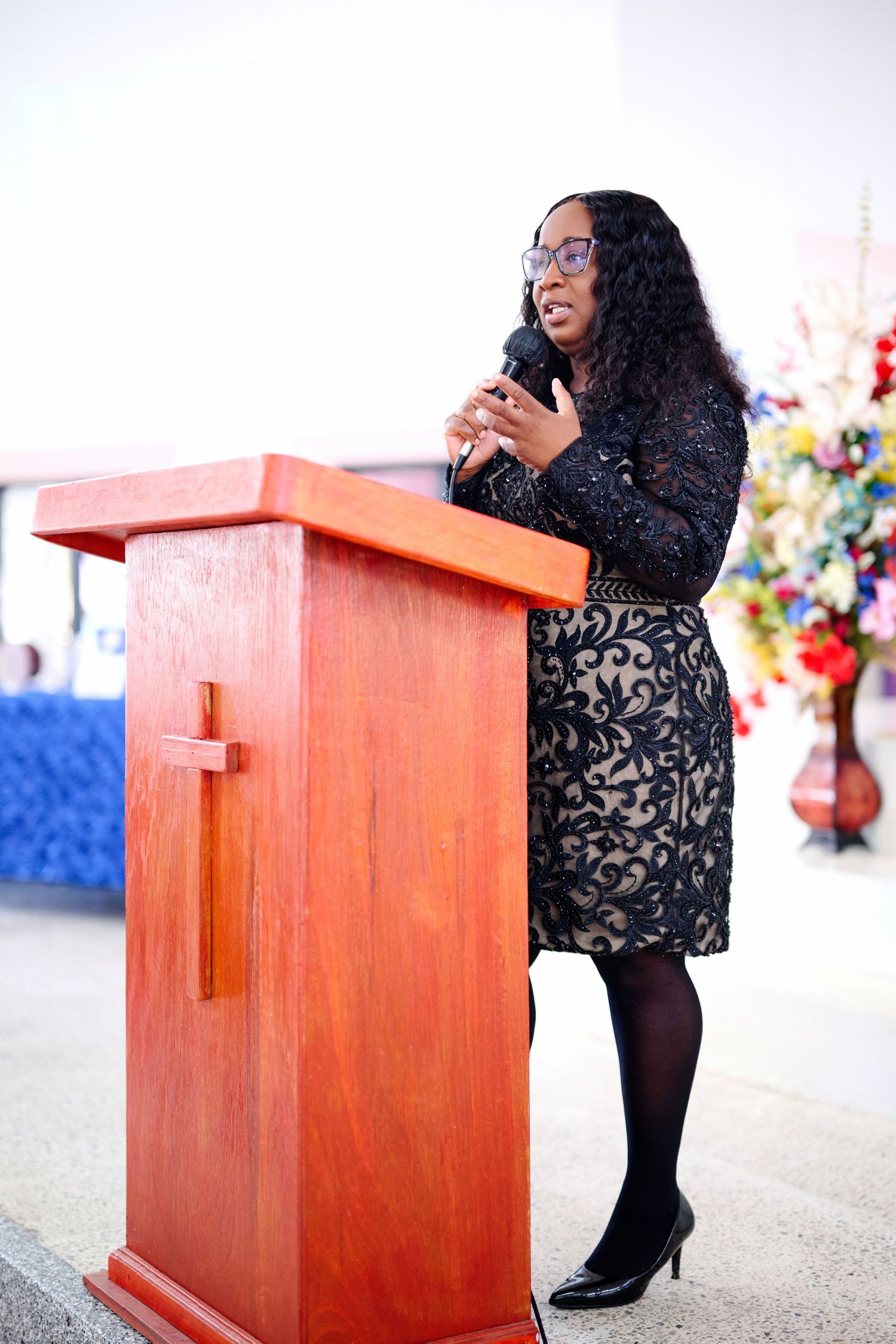 Speaker in black lace dress presenting at wooden podium during ceremony.