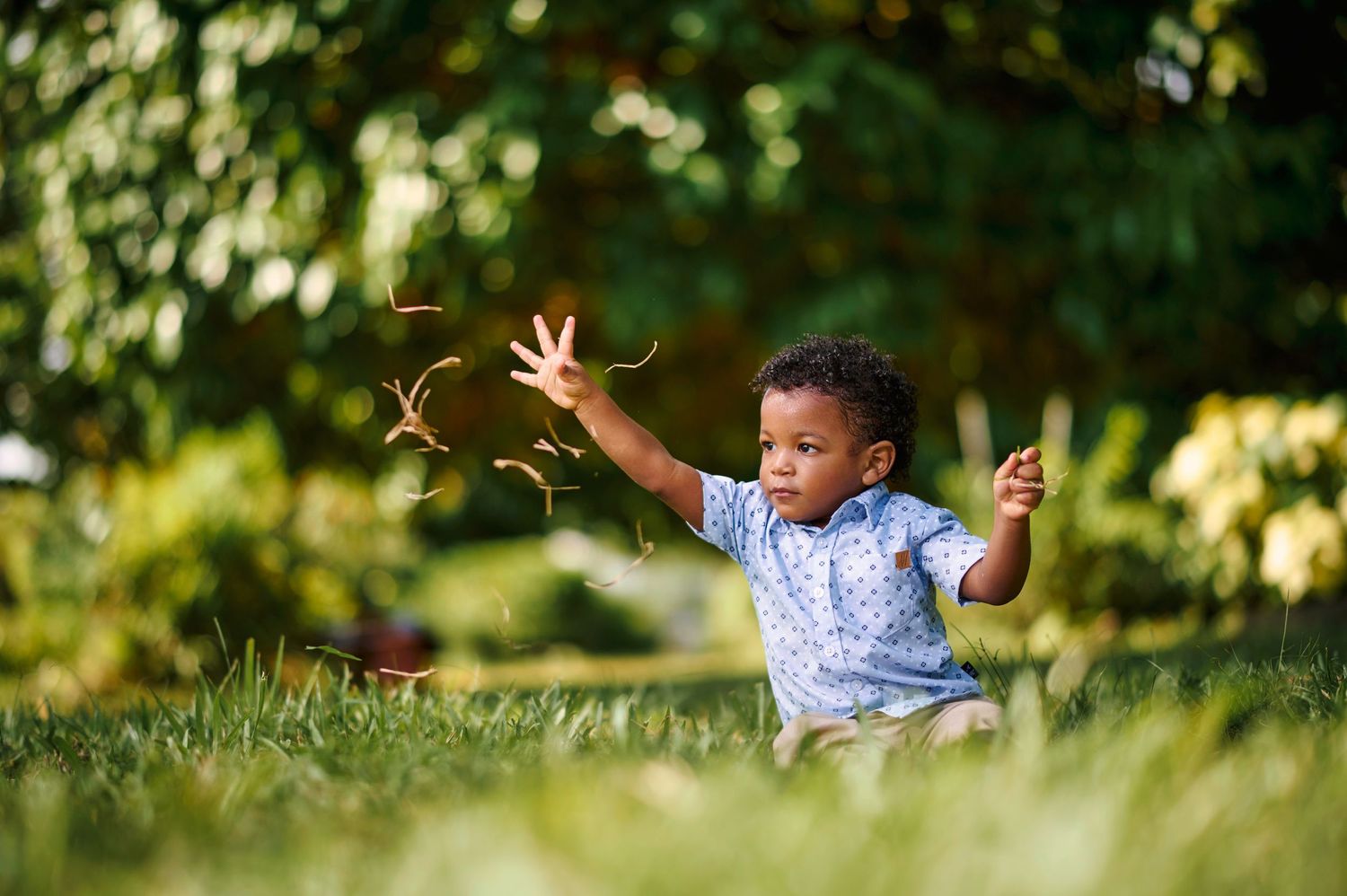 Young child playing outdoors in a grassy area with natural sunlight filtering through trees.