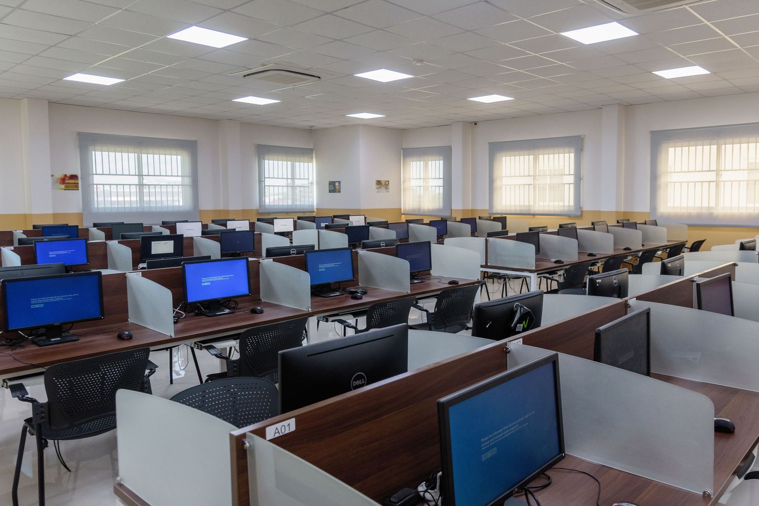 Modern computer lab with rows of empty workstations and fluorescent lighting.