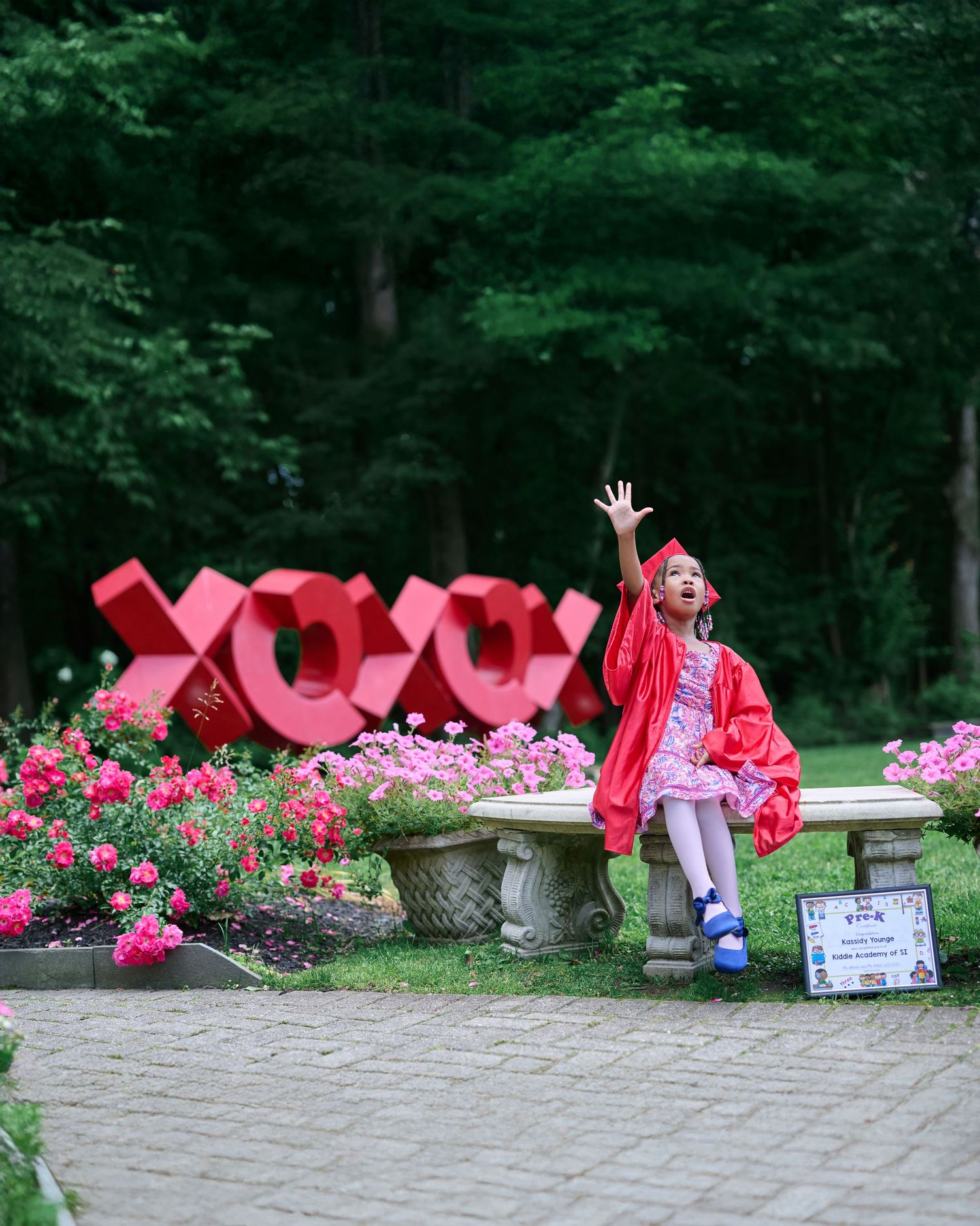 Creative graduation photo sequence with red cap and gown near pink flower garden.