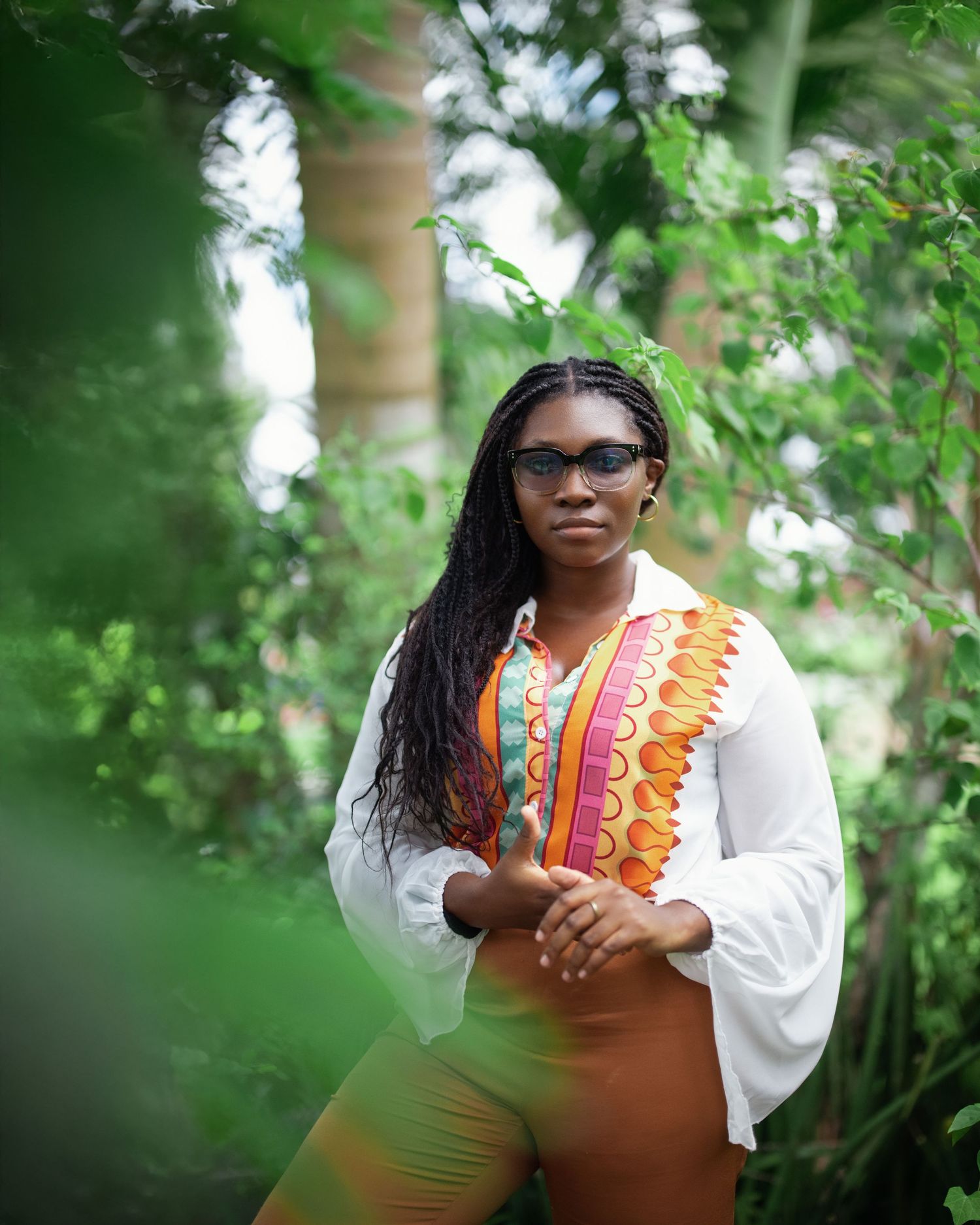 Casual portrait in orange and white patterned top among green foliage.