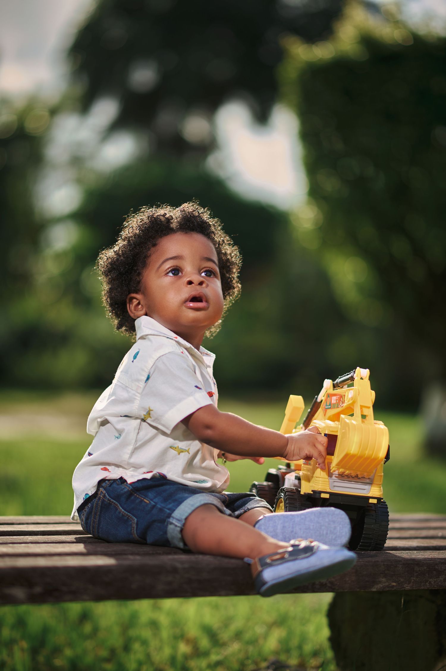 Child playing with yellow toy construction vehicles while sitting on wooden bench.