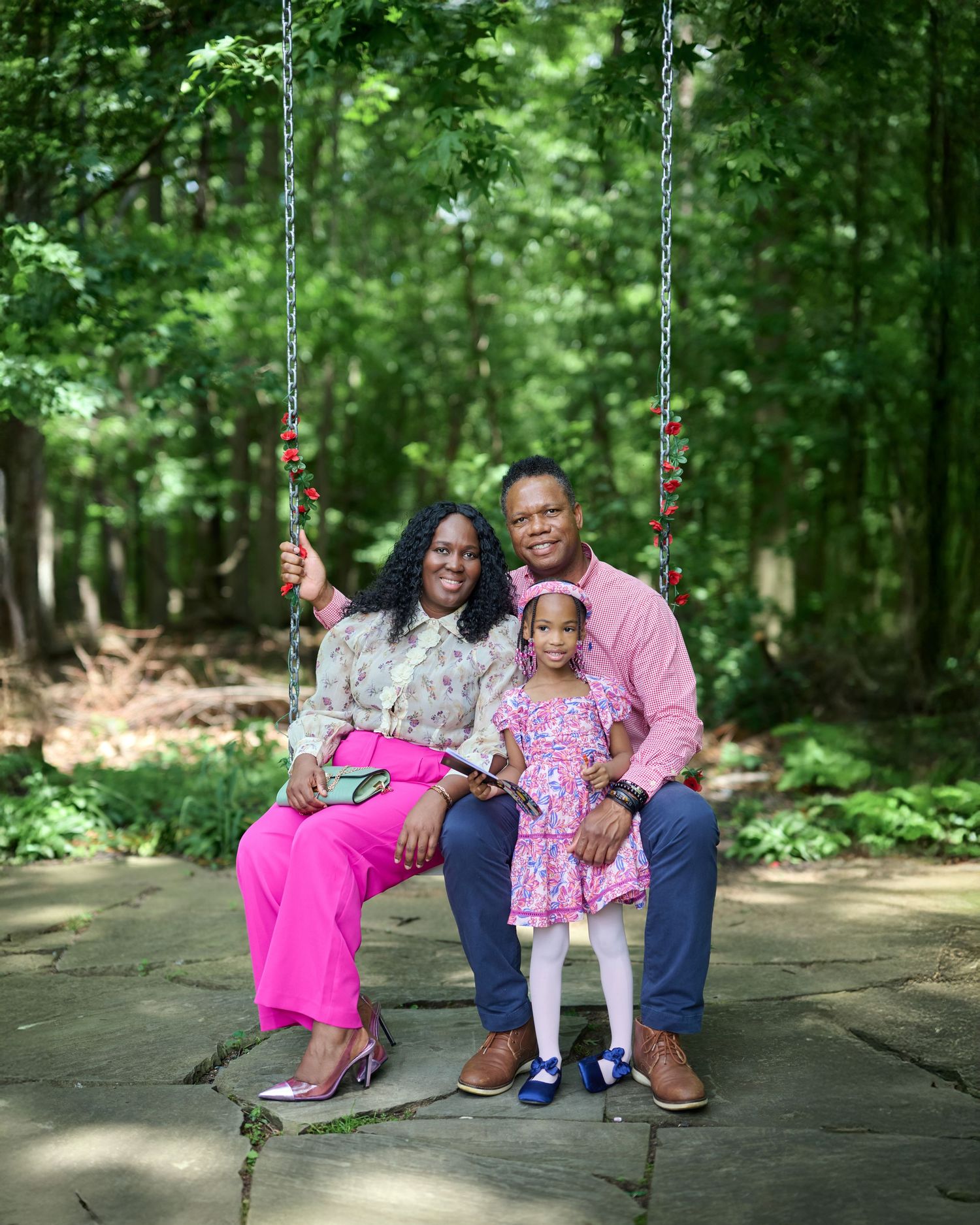 Outdoor portrait session on a swing set surrounded by lush green forest.