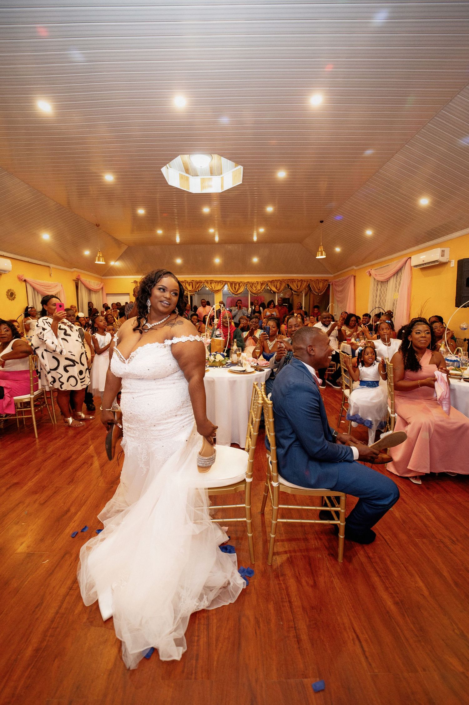 Wedding reception celebration with dancing on a polished wooden floor under warm lighting.