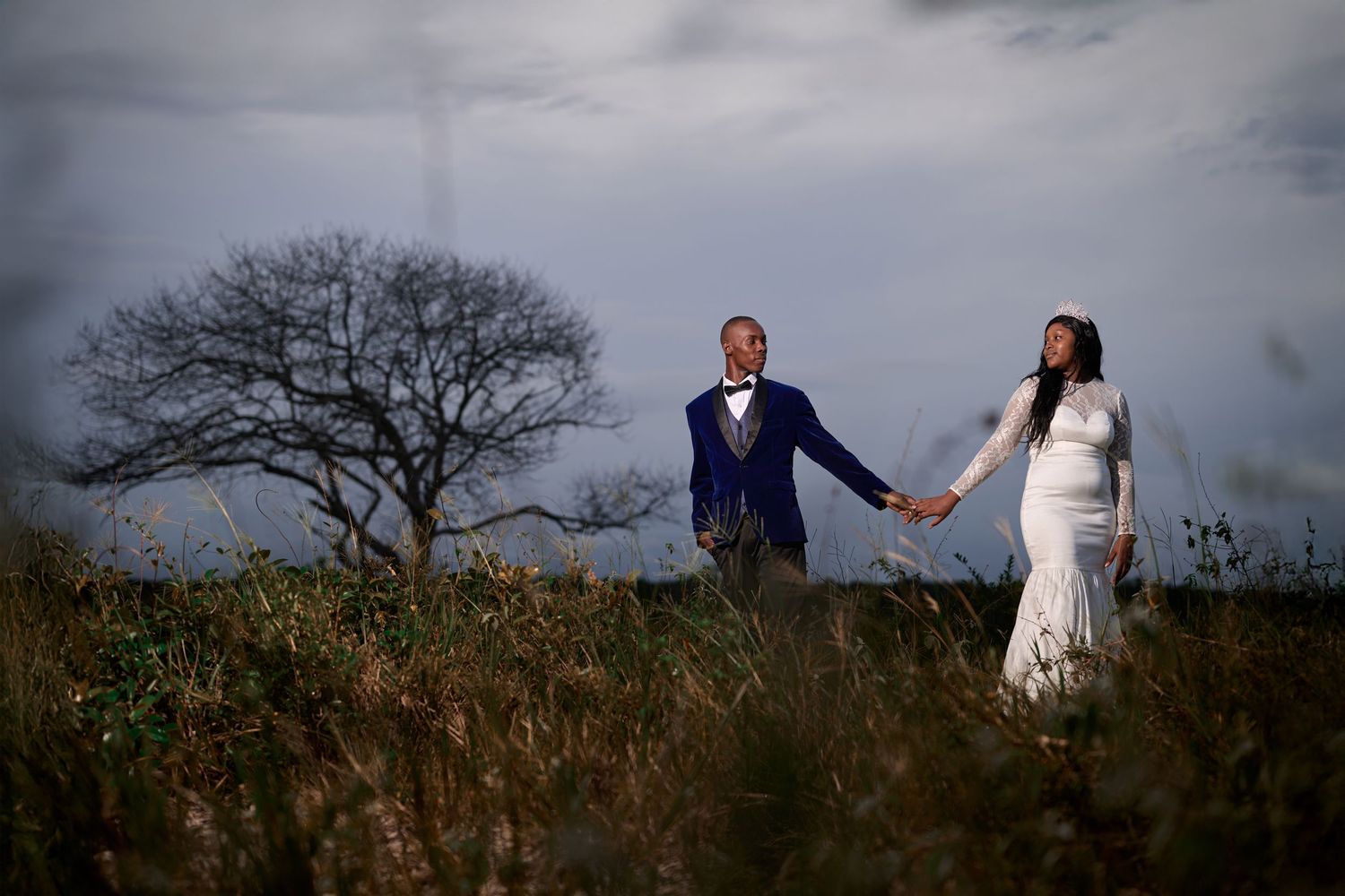Silhouetted couple walks along hilltop ridge during dramatic sunset wedding shoot.
