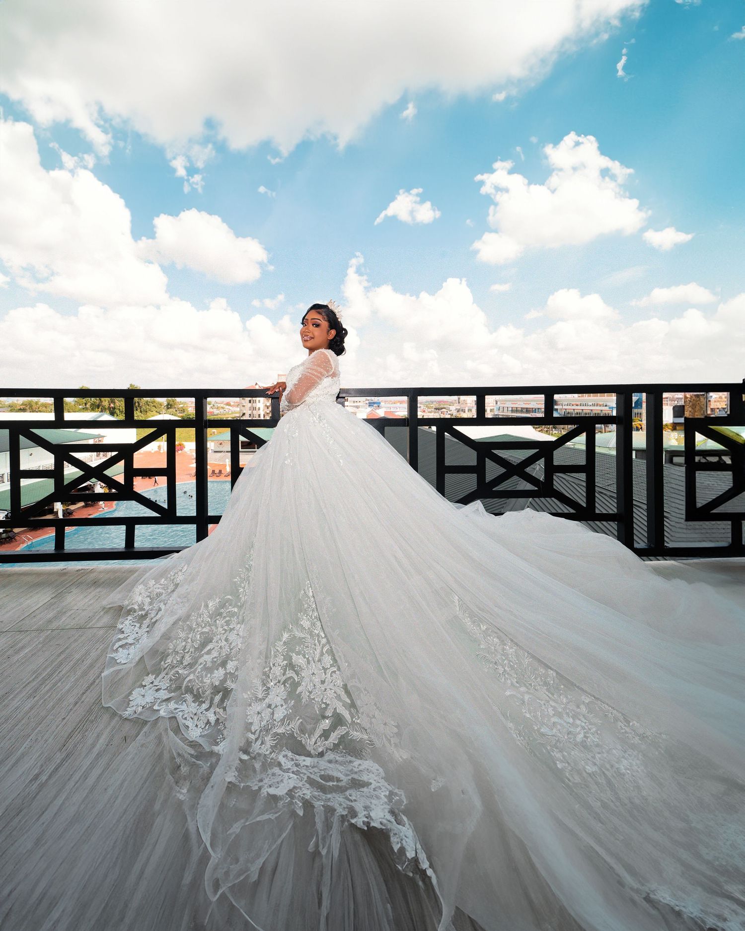 Flowing white wedding dress with intricate lace details against blue sky and railing.