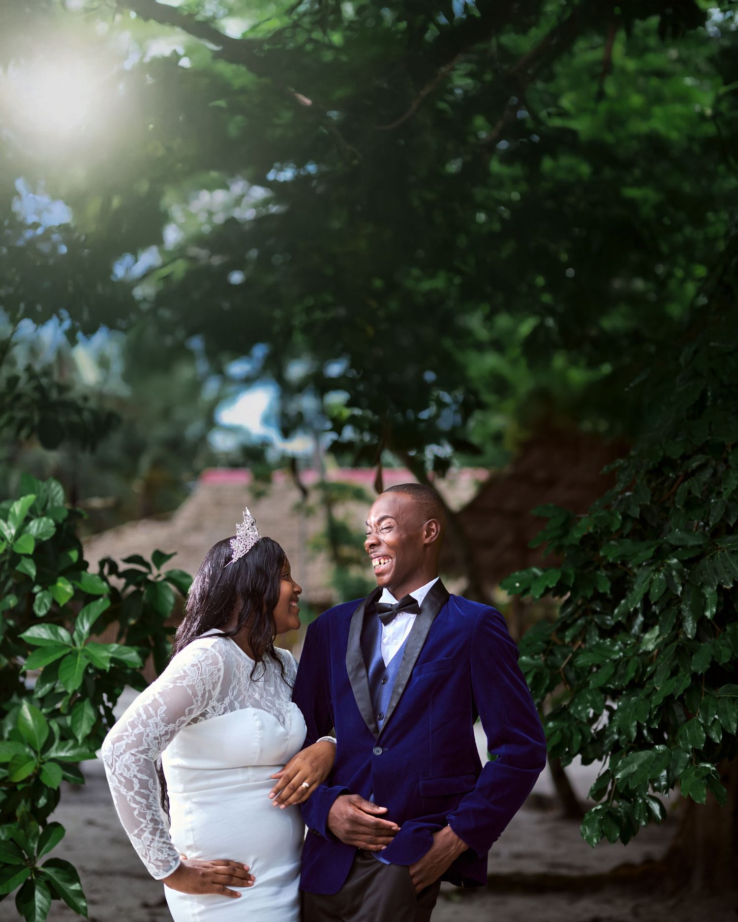 Wedding couple laughs together surrounded by green foliage in a garden setting.