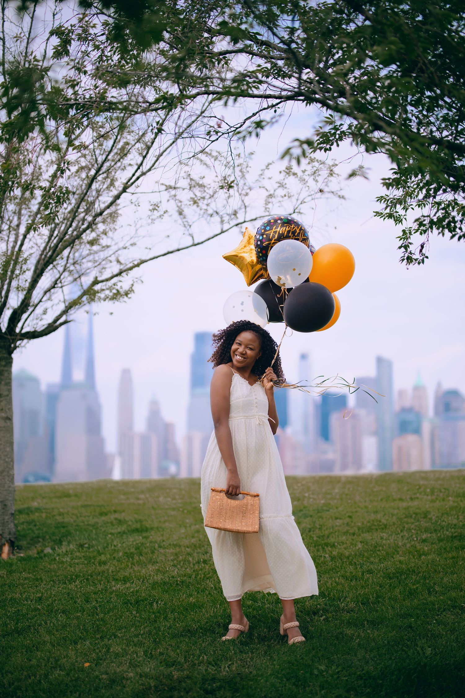 Person with balloons poses playfully against Chicago skyline on grassy hill.