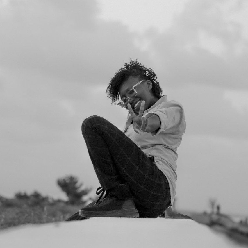 Black and white portrait of person in casual wear sitting in contemplative pose outdoors.