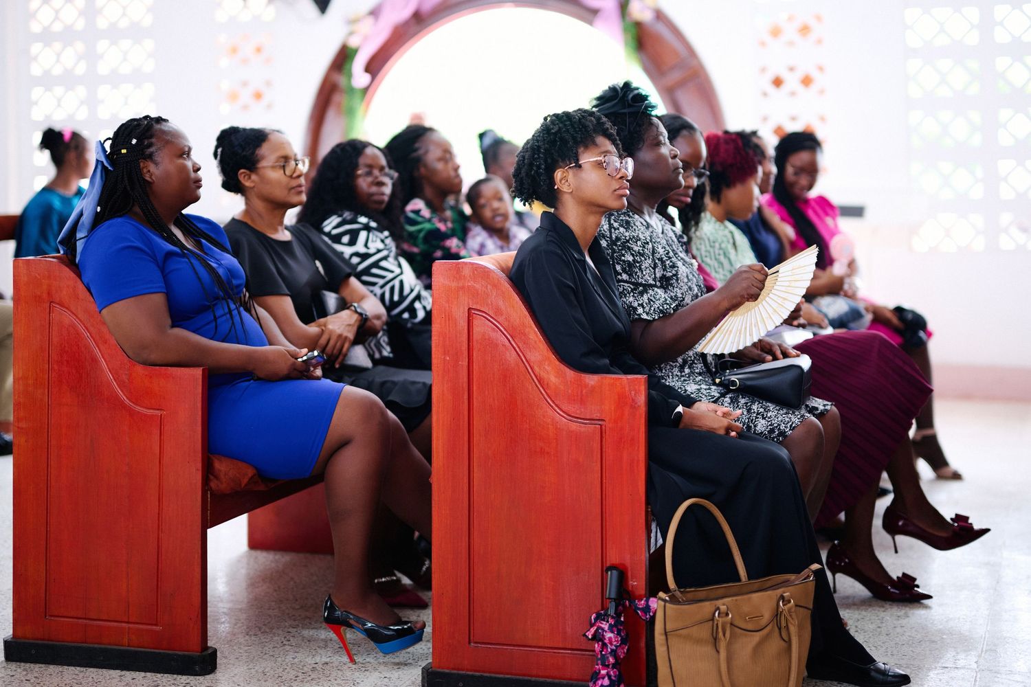 Audience members seated in red chairs during indoor event.