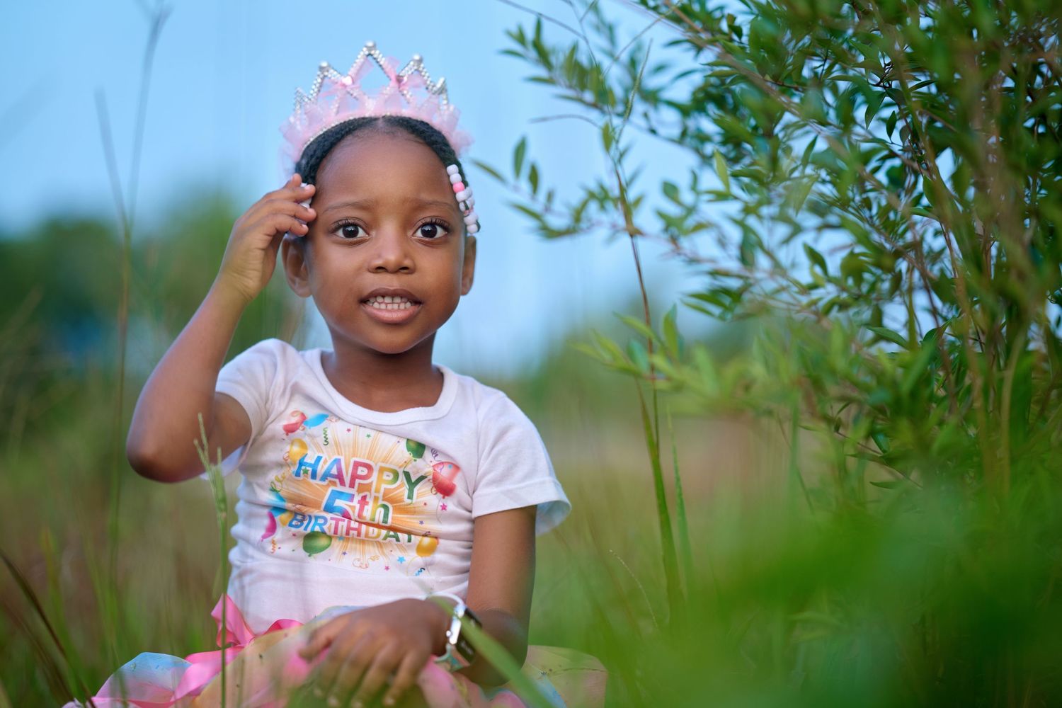 Young child playing outdoors among green foliage on sunny day.