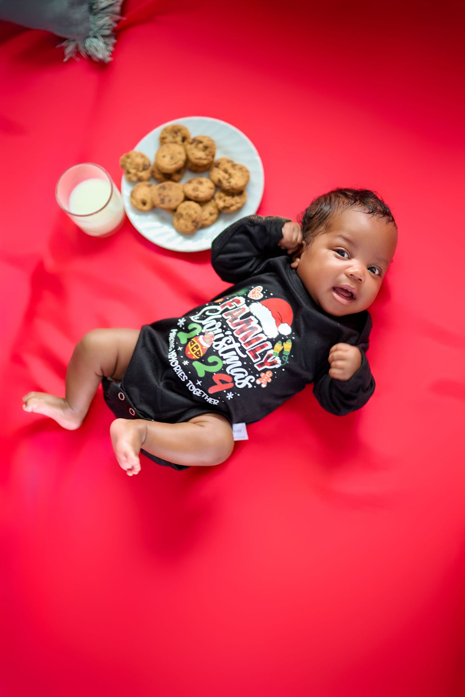 Christmas themed baby photo with milk and cookies on vibrant red background.