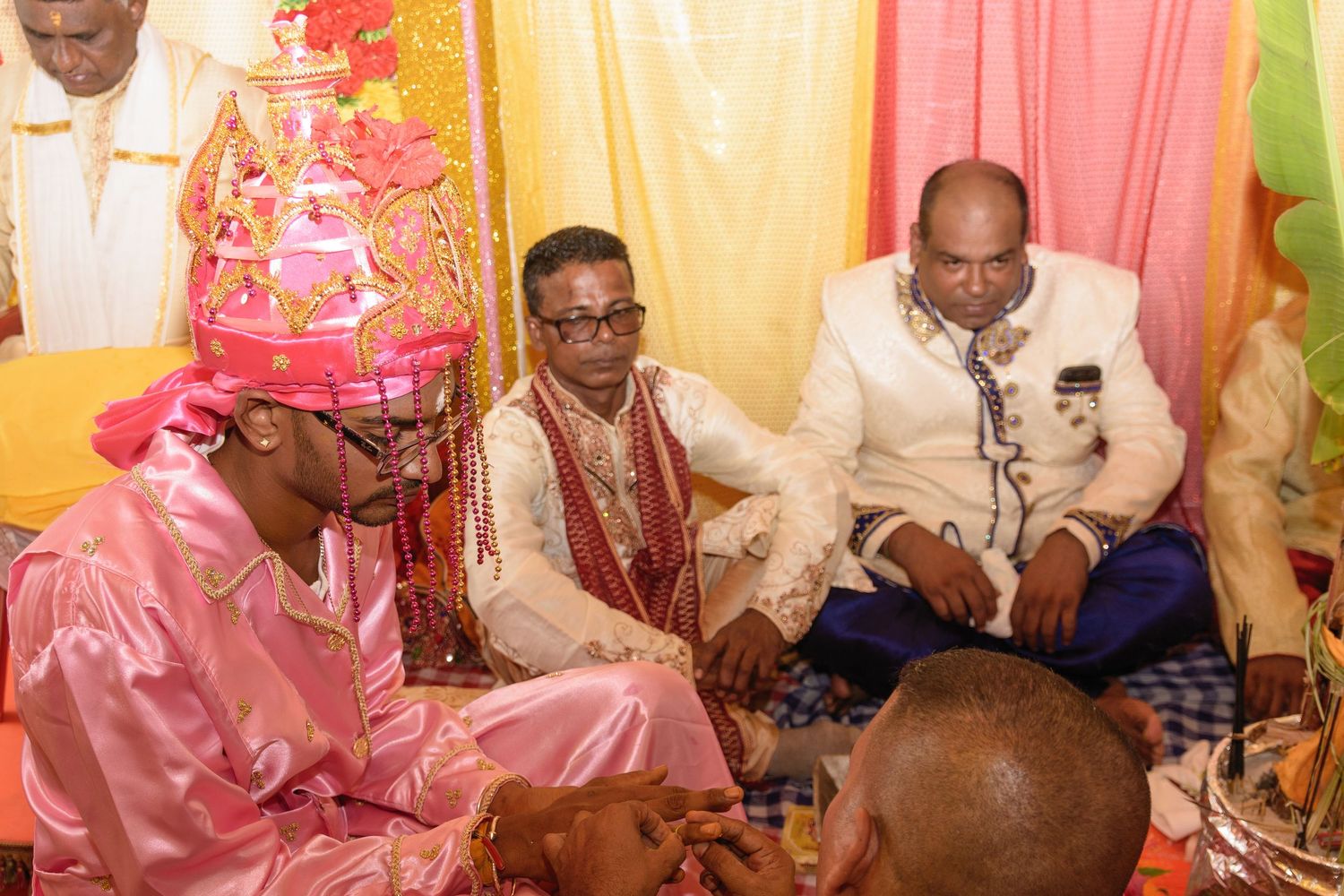 Wedding ceremony guests seated in a decorated venue with pink and yellow fabric draping.