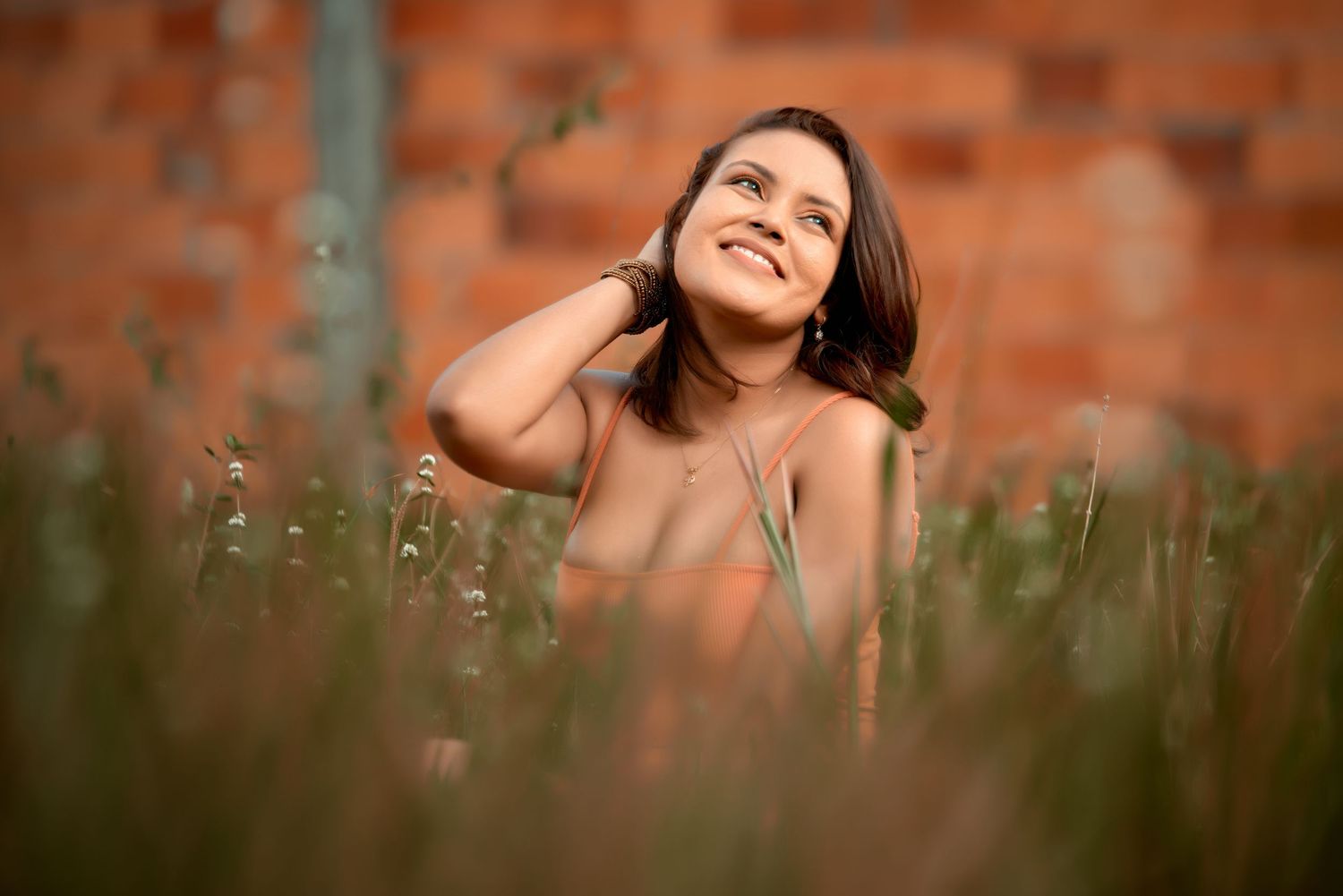 Figure in orange dress sitting against rustic brick wall background during golden hour photography session.