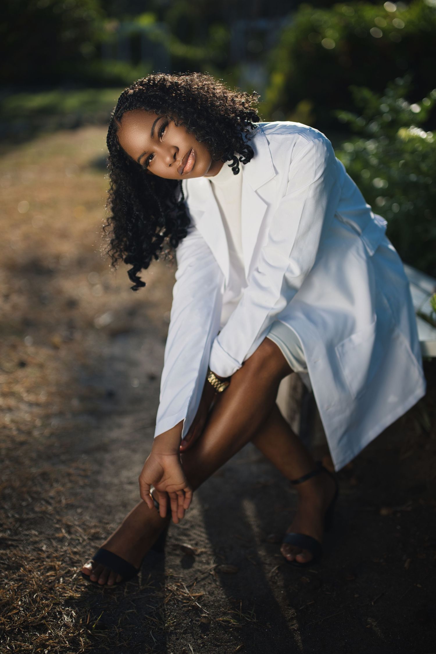 Person in white dress bending down outdoors in artistic lighting.