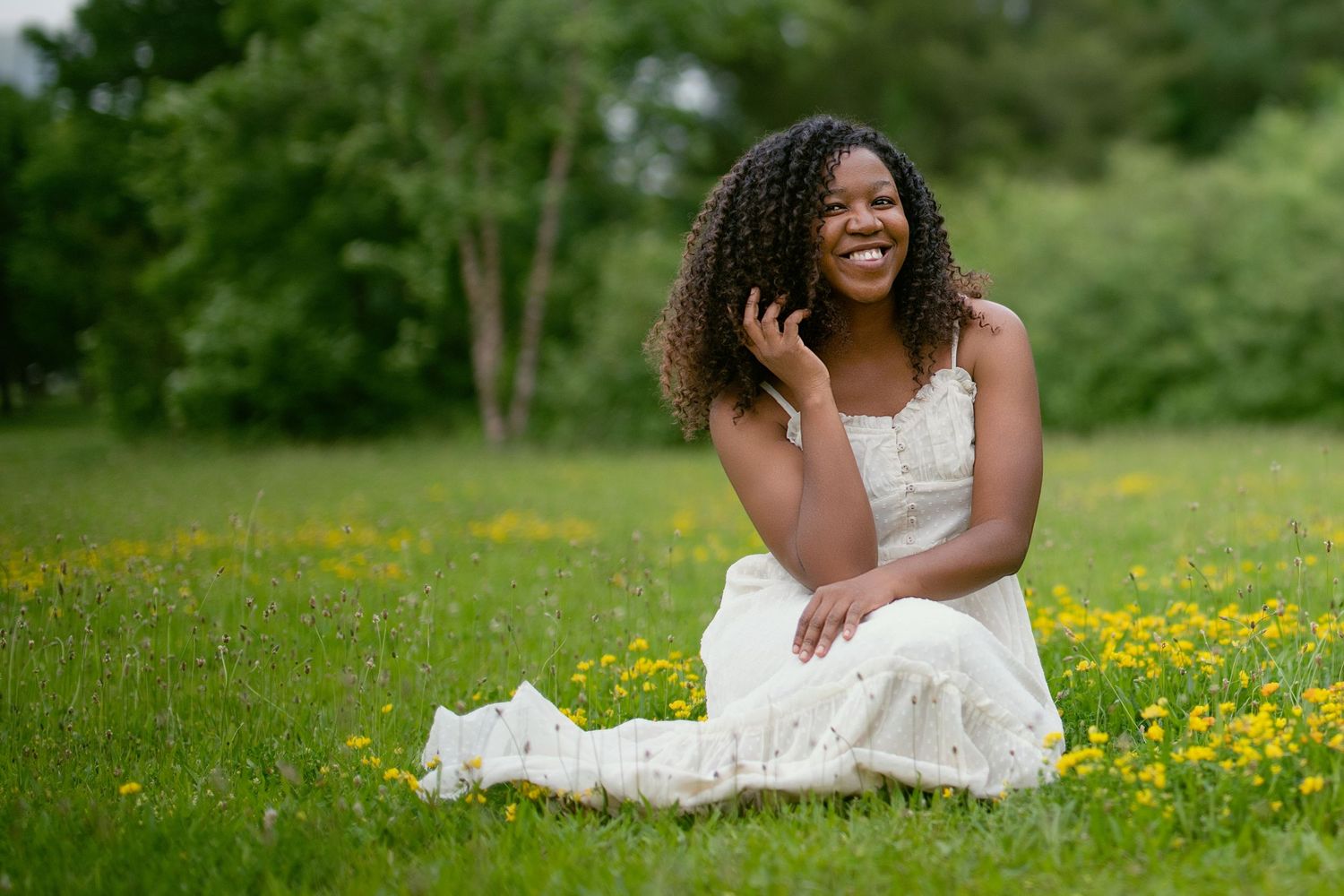 Person in white dress posing gracefully on grass surrounded by yellow flowers in a garden setting.