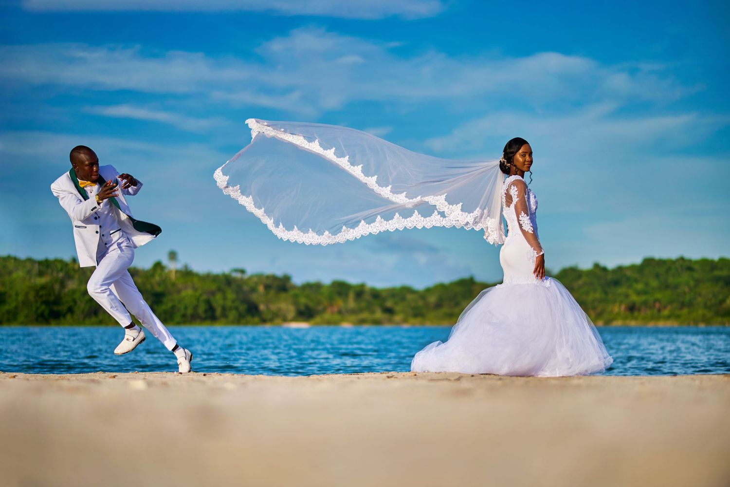 Creative beach wedding photo with couple pulling white veil across sandy shore.