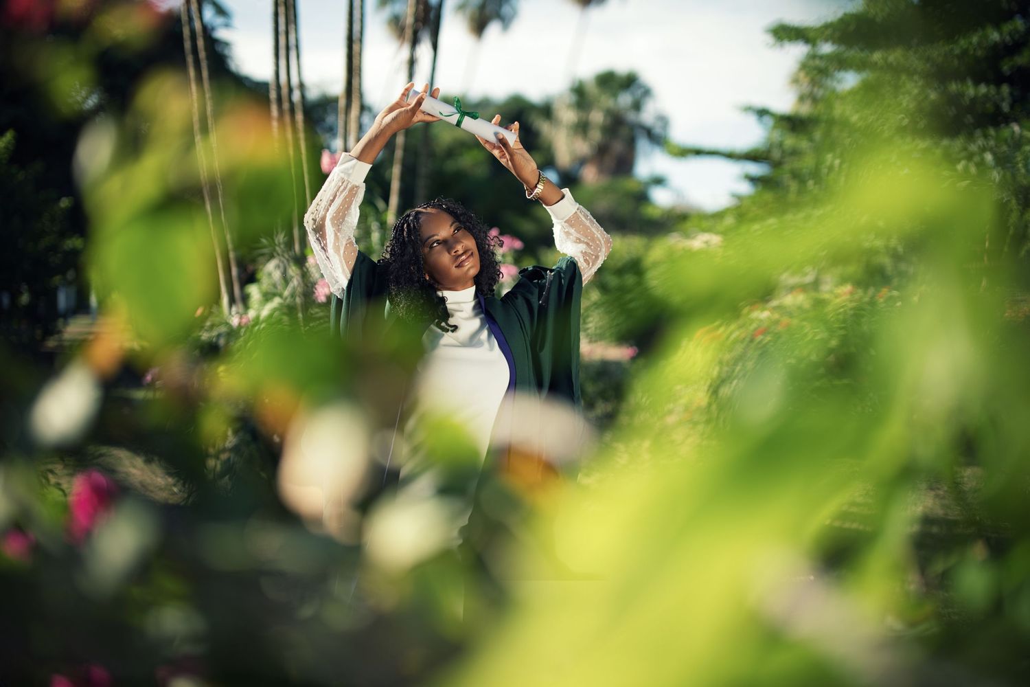 Artistic graduation photoshoot through green foliage in garden setting.