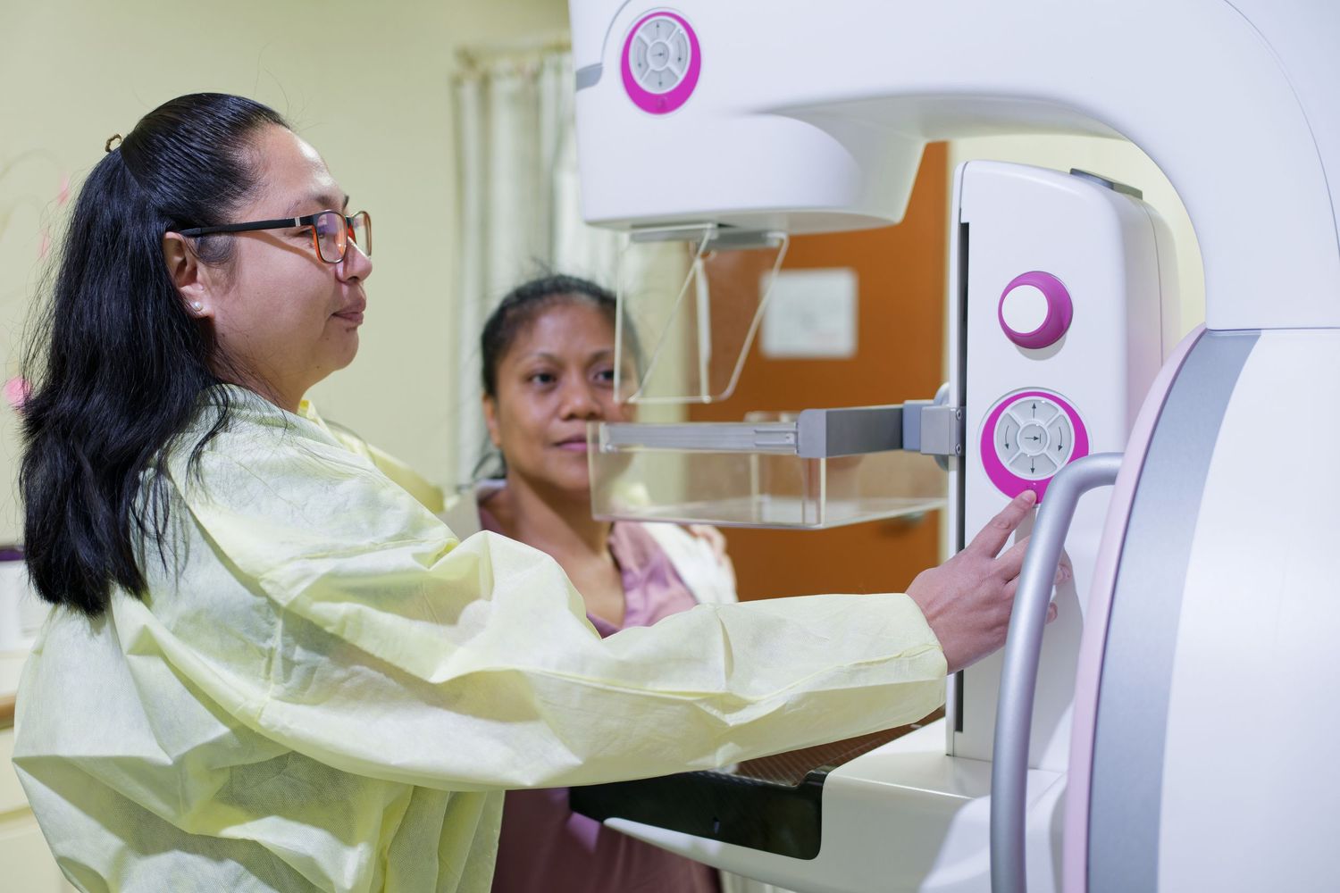 Patient receiving mammogram screening with medical technologist assistance.