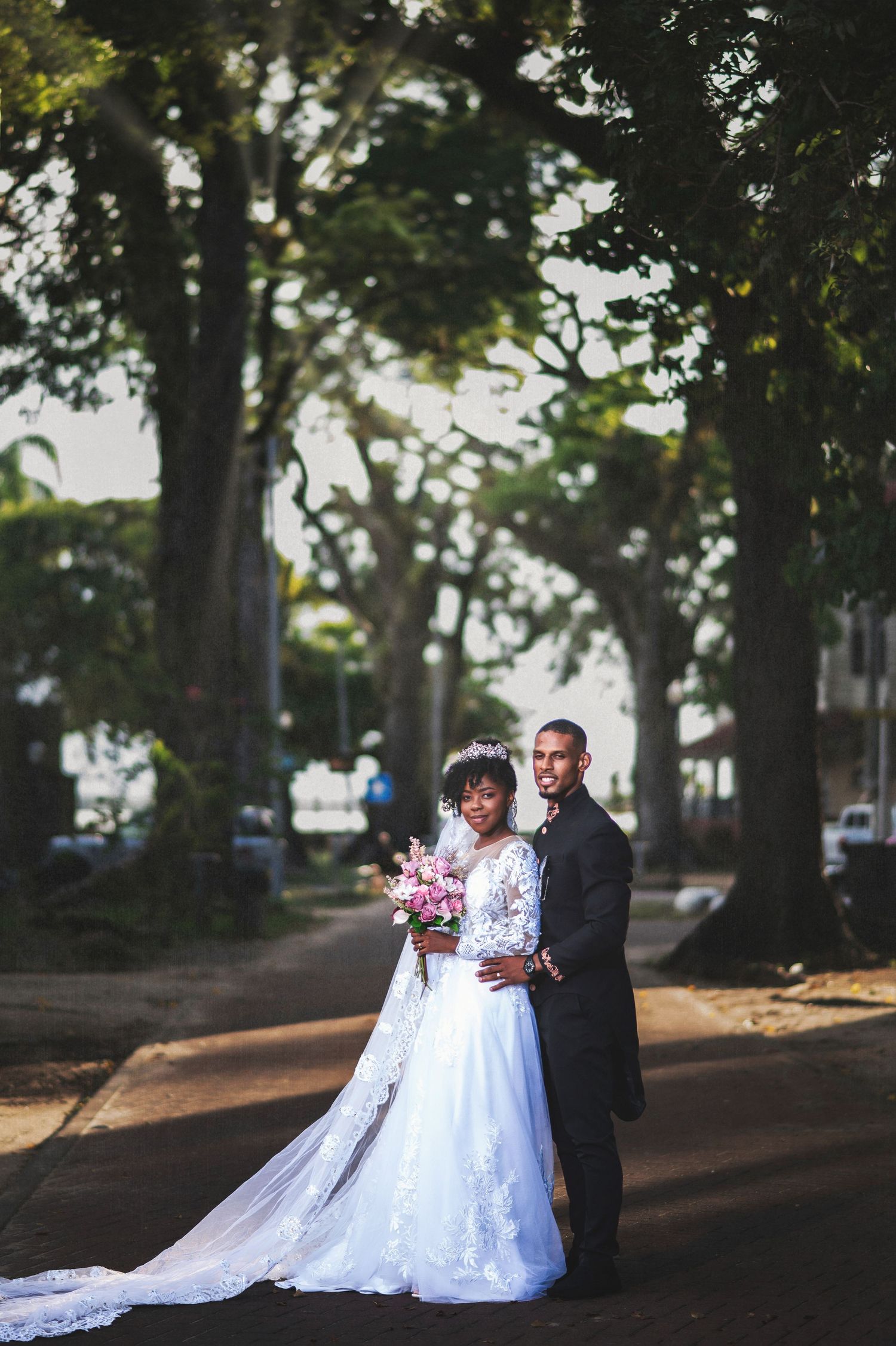 Wedding couple poses under shaded trees in a romantic outdoor setting.