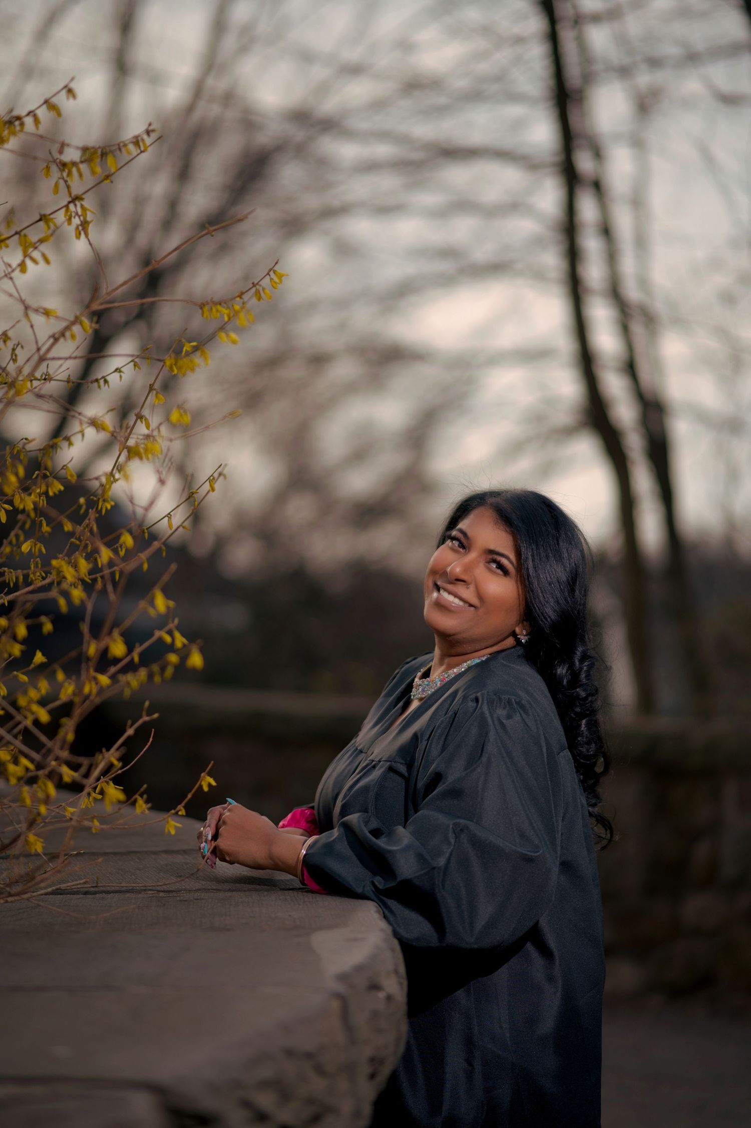 Graduation photo session with someone playfully posing among bare trees.