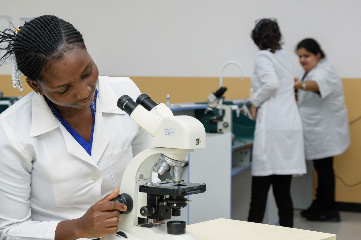 Laboratory technicians in white coats working with microscopes and scientific equipment in a research facility.