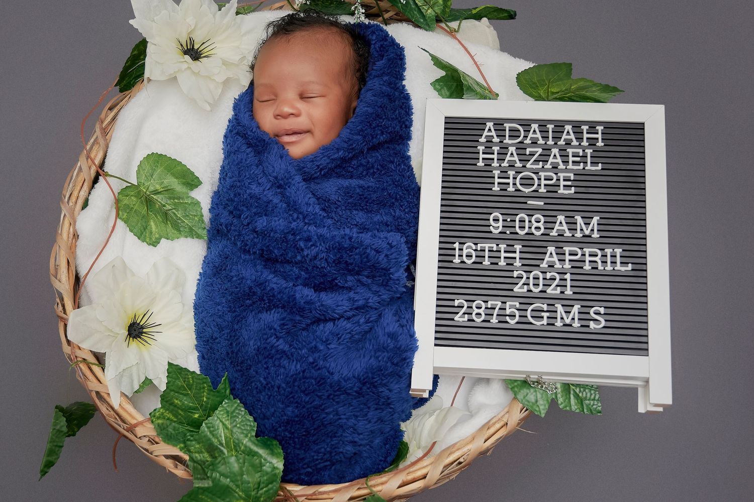 Sleeping newborn in basket with birth details displayed on letter board.
