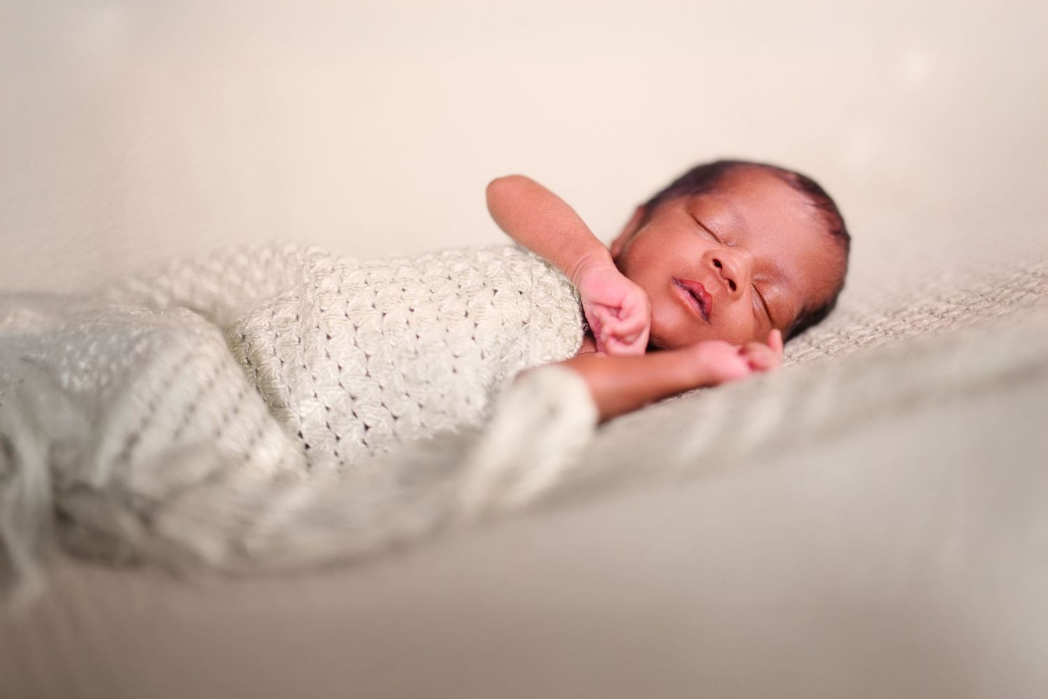 Sleeping newborn wrapped in delicate white lace blanket.