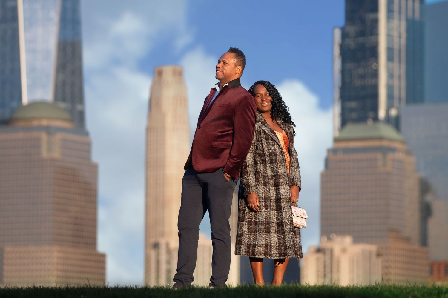 Two people embrace against the dramatic Manhattan skyline on a sunny day.
