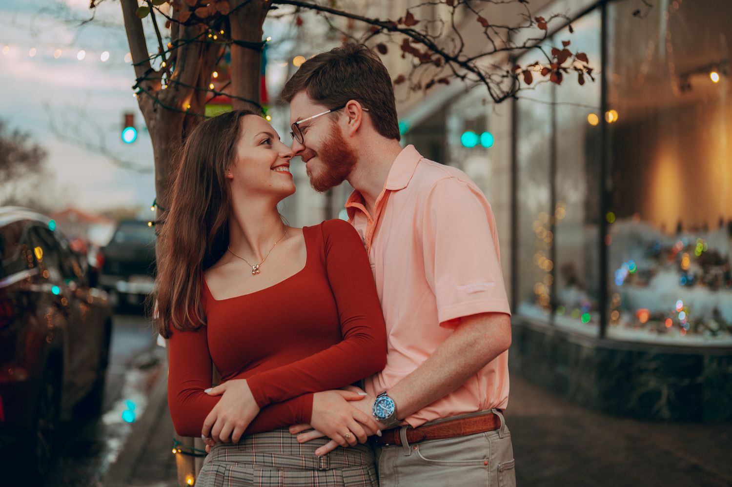 Romantic couple nearly kissing under festive string lights in a colorful outdoor setting.