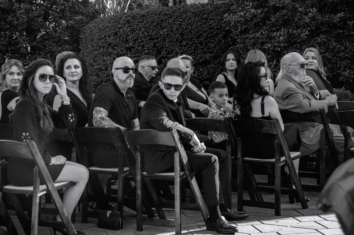 Black and white photo of wedding guests seated in chairs during outdoor garden ceremony.