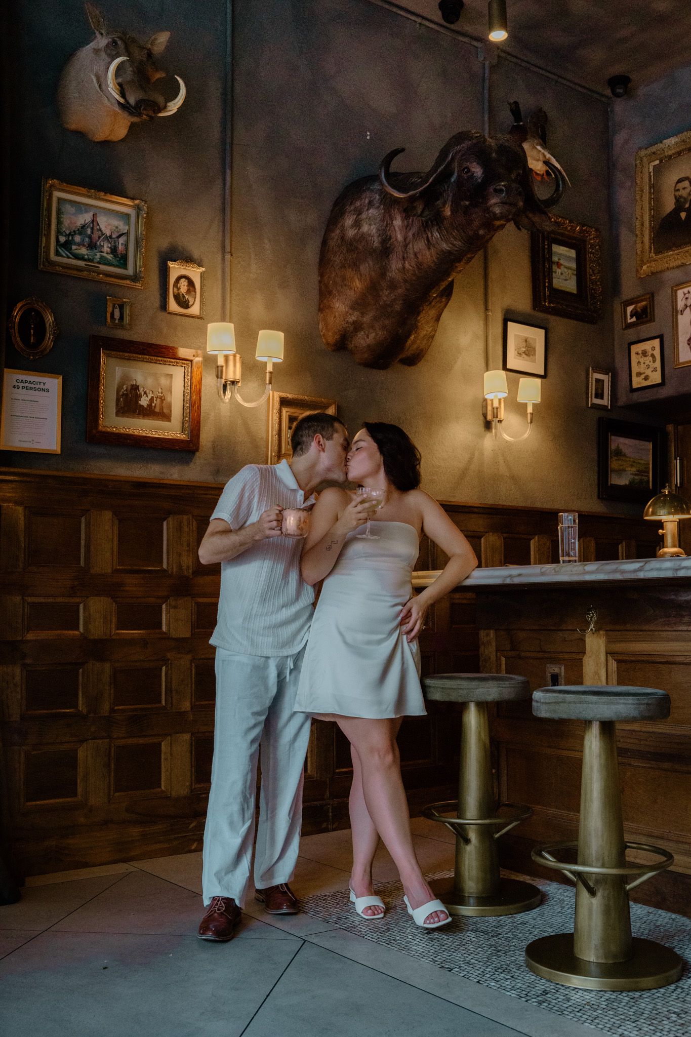 Couple kissing near a bar in a dimly lit rustic restaurant with taxidermy wall decor.