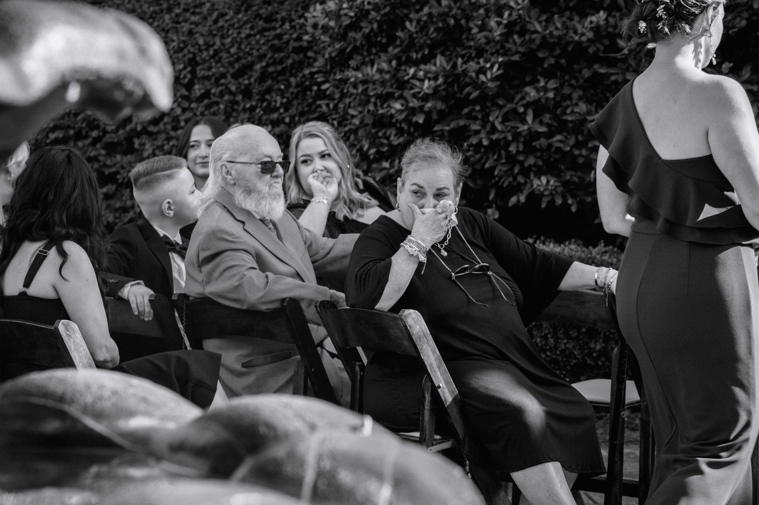 Emotional wedding guests crying and comforting each other during outdoor ceremony in black and white photo.