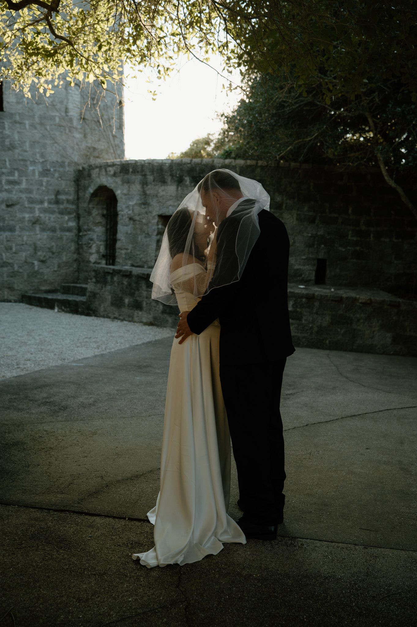 Bride and groom share a kiss under a veil at Castle Ottis venue during golden hour wedding portraits.