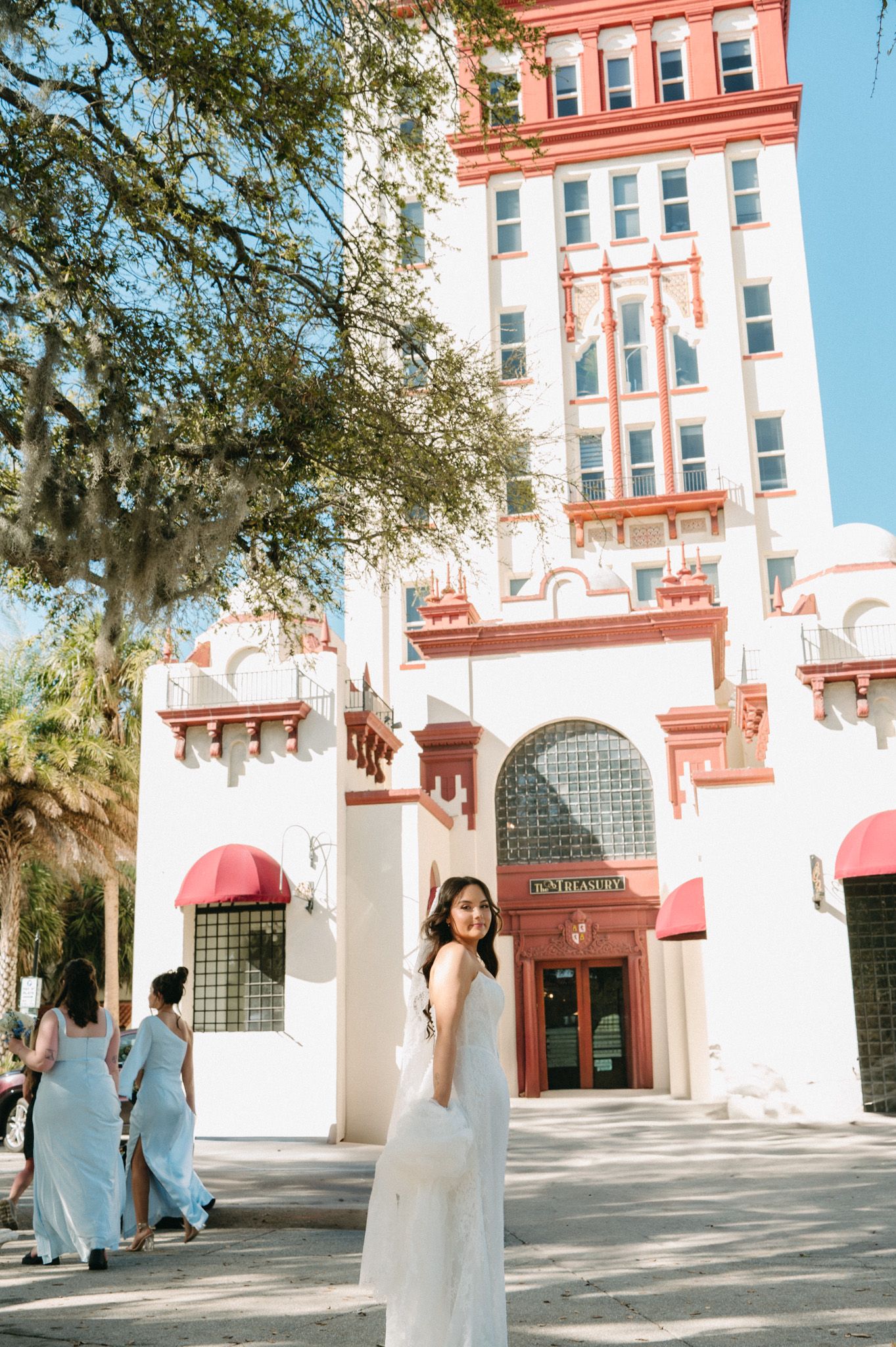 Bride in white gown poses in front of historic red and white Treasury building in St. Augustine.