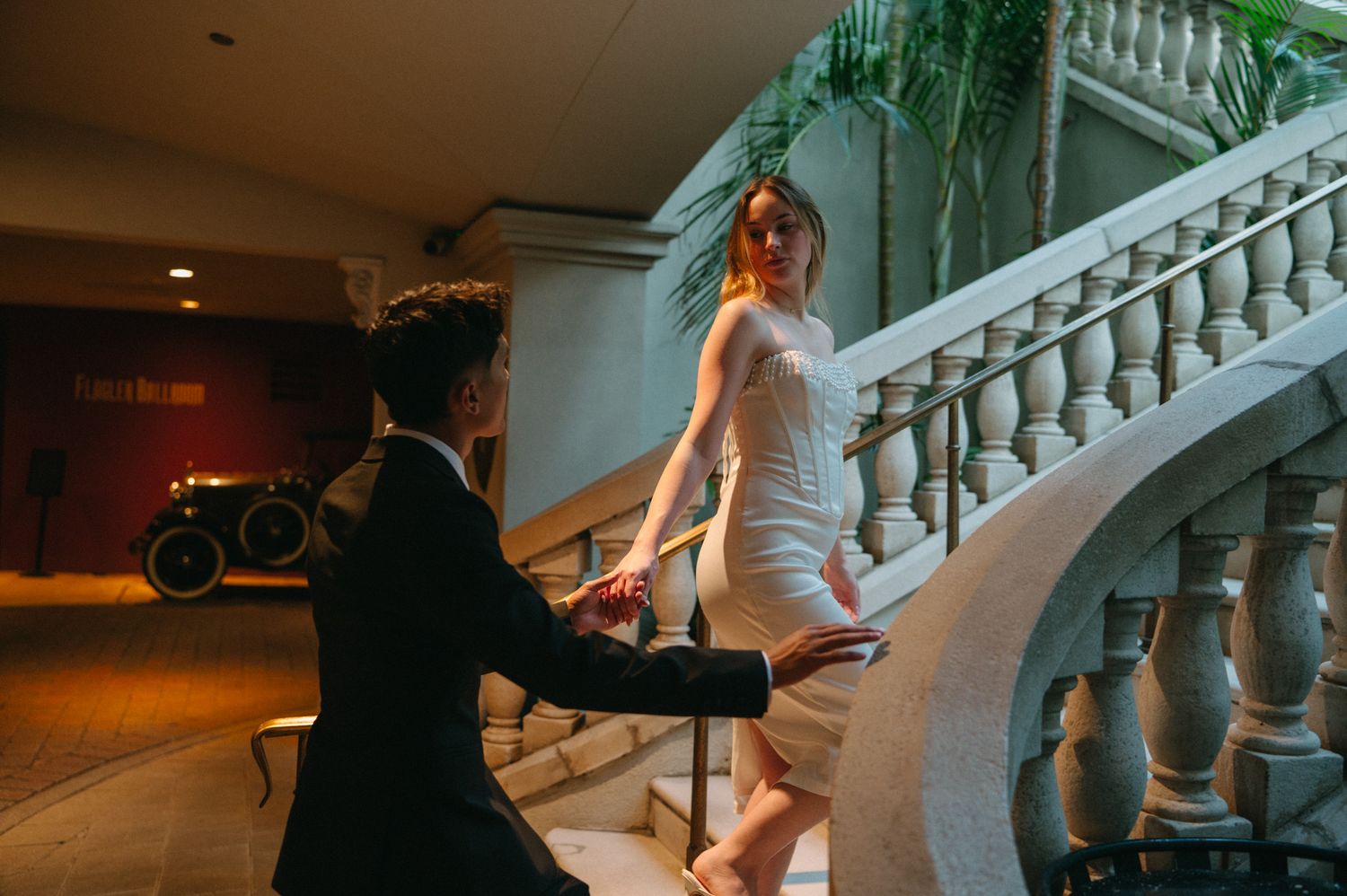 Groom holding bride's hand as she descends grand white marble staircase in wedding dress in downtown St. Augustine, FL.