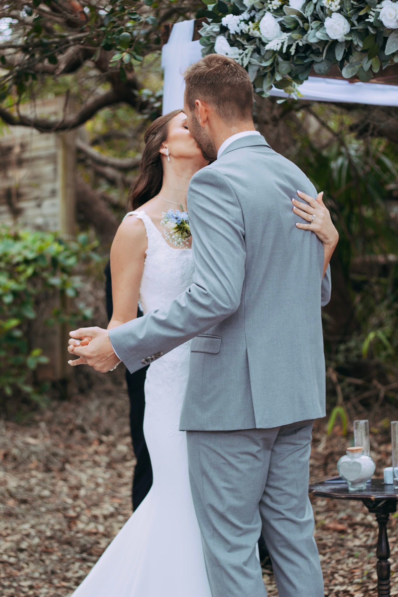 Newlyweds share first kiss under floral arch at outdoor garden wedding ceremony.