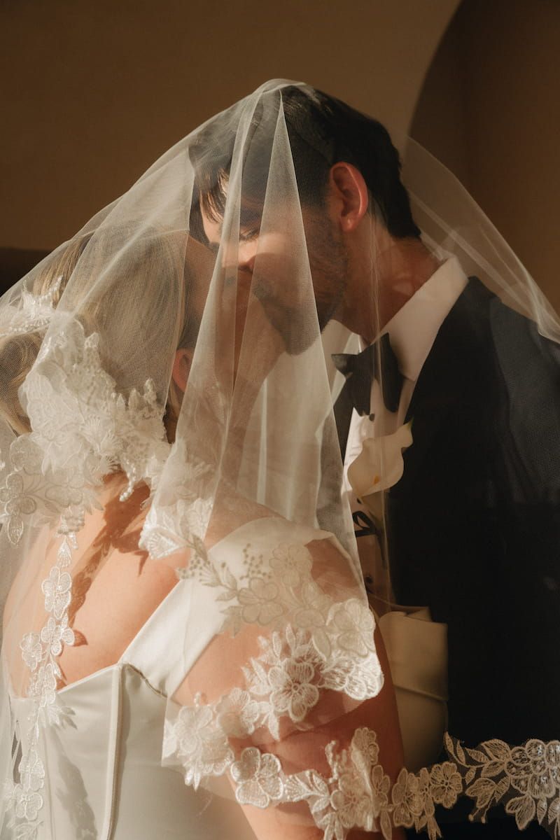Bride and groom sharing a romantic kiss under a lace wedding veil during their ceremony.