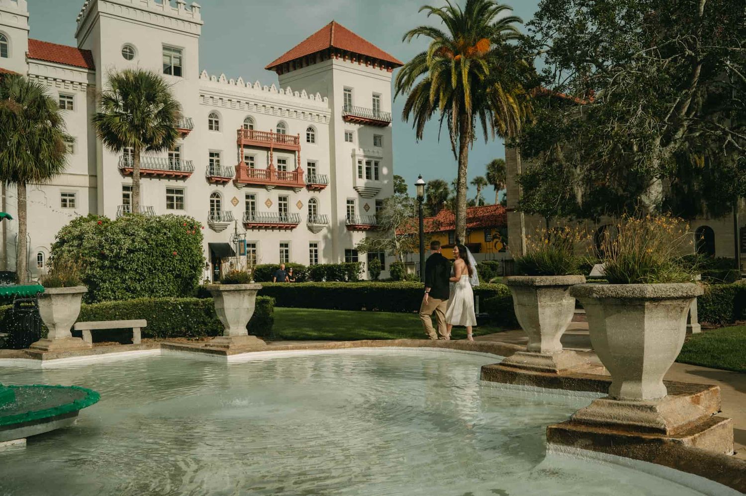 Couple embracing near a fountain at Casa Monica Resort in St. Augustine, Florida, surrounded by lush palms and elegant architecture.