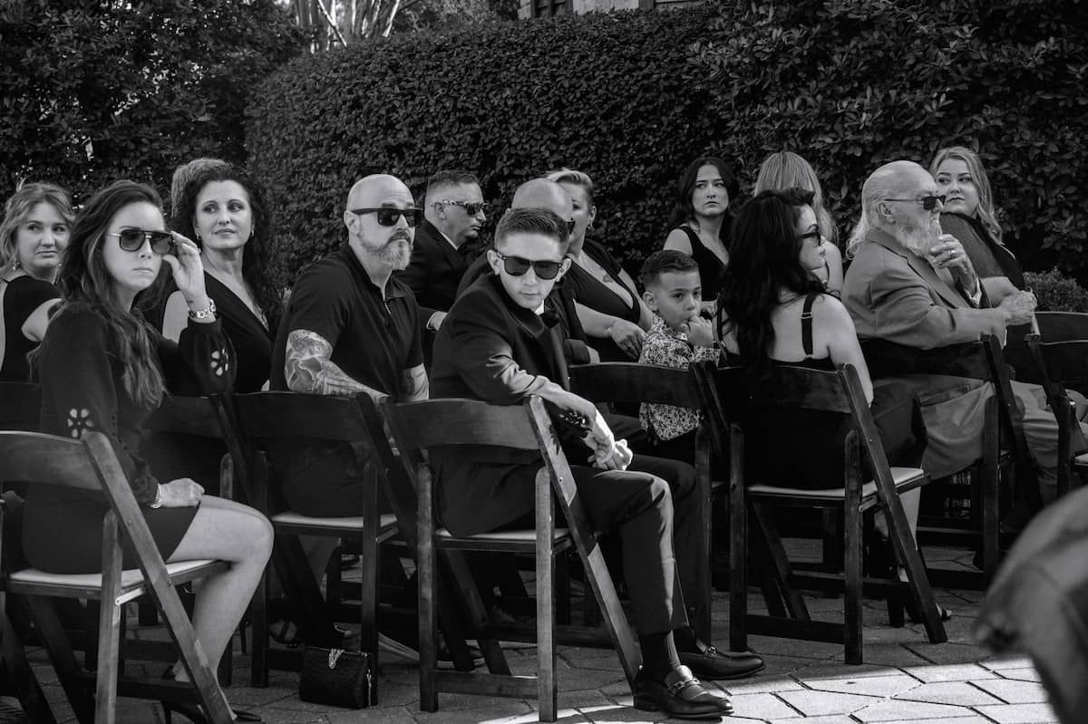 Black and white photo of elegantly dressed guests seated outdoors at a formal event or ceremony.