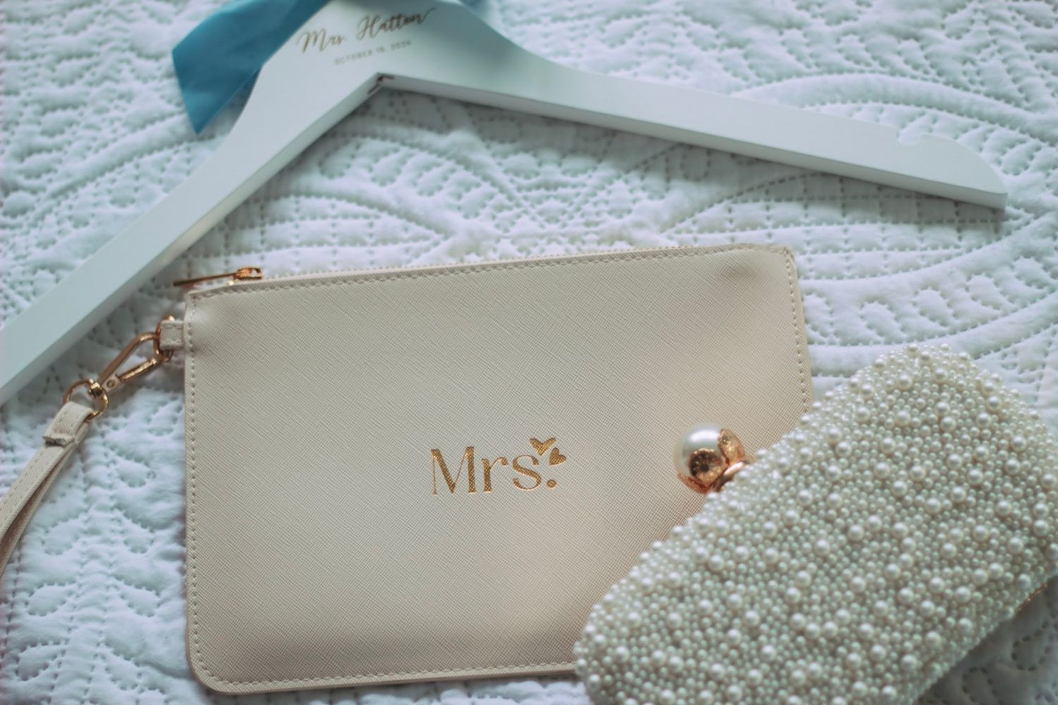 Wedding day accessories including Mrs. clutch purse and pearl bag on white quilted surface.