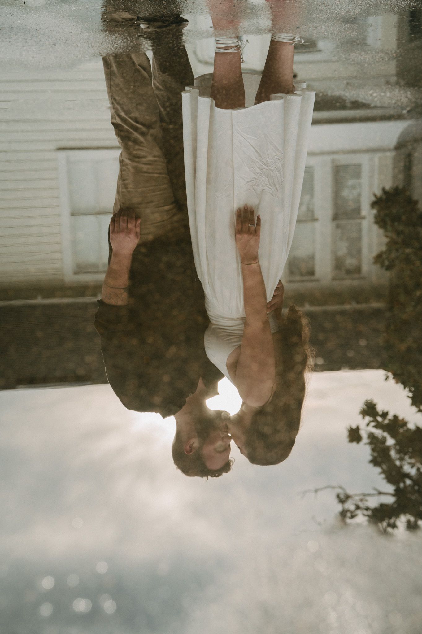 Creative reflection photo of wedding couple kissing captured in puddle on ground.